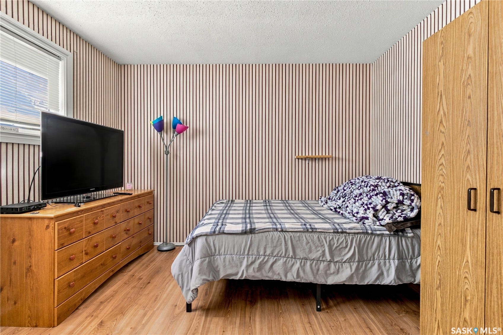 Hardwood-style flooring, striped wall covering, window with blinds, and built-in closet