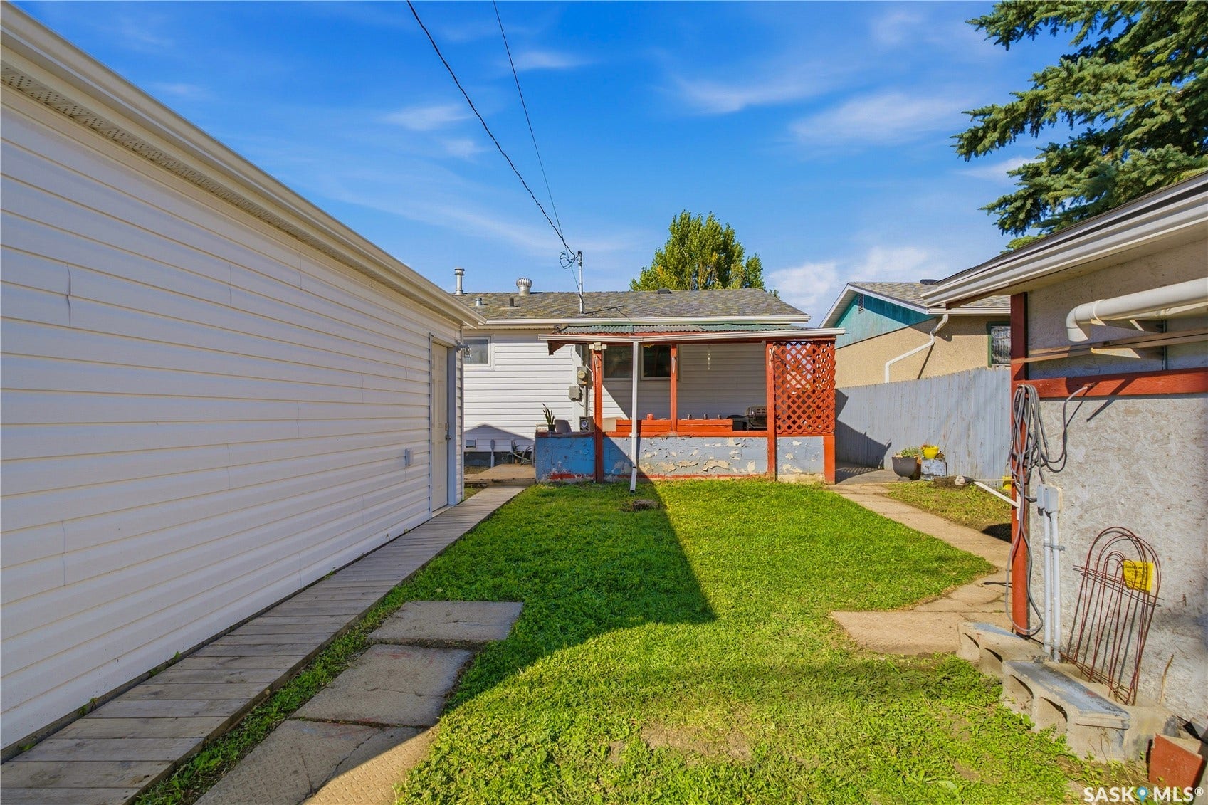 Backyard featuring a covered patio with red lattice, a detached garage with white siding, and a grass lawn
