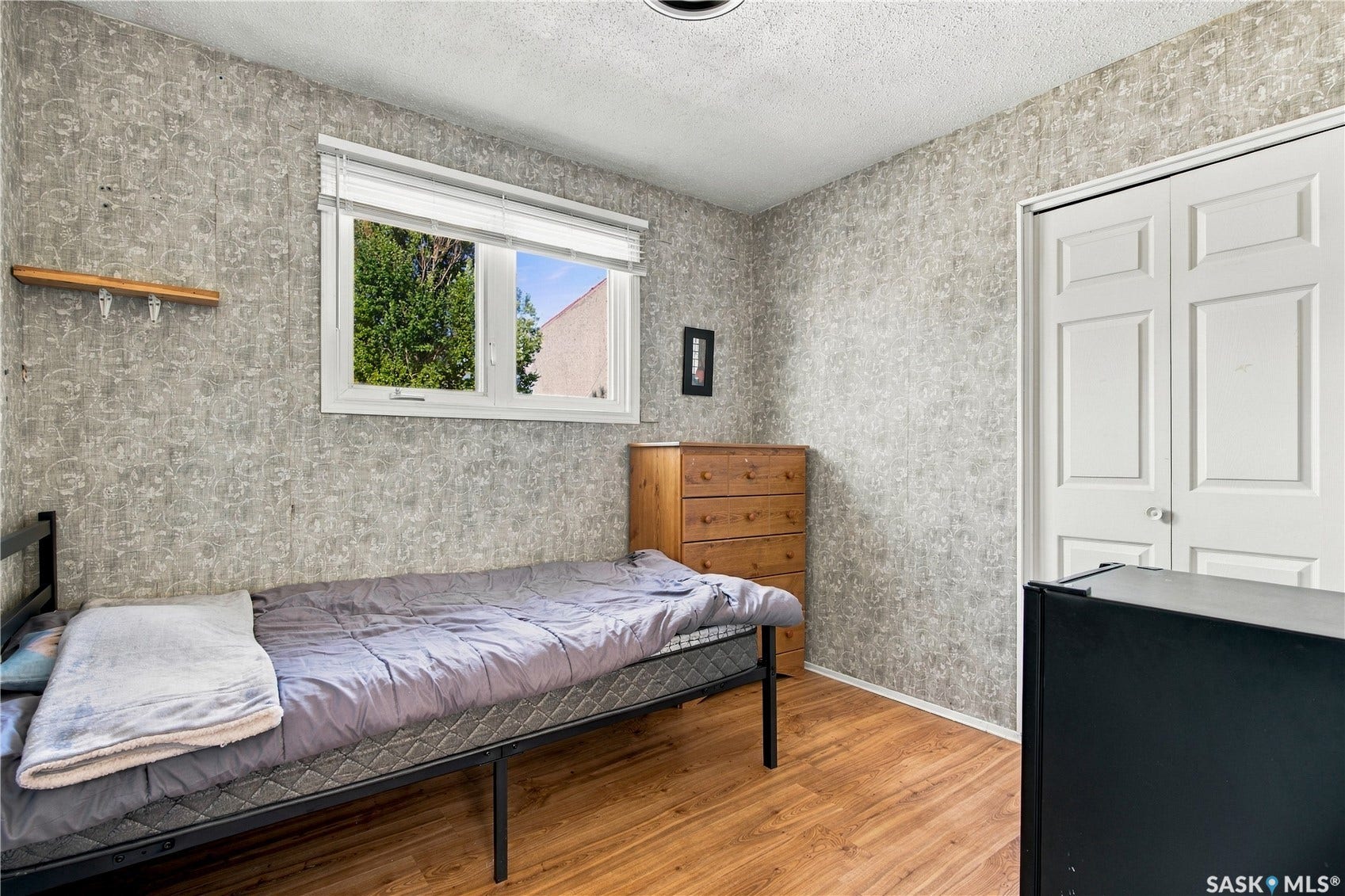 Wood-finish flooring, textured wallcovering, double-panel closet doors, and a window with blinds