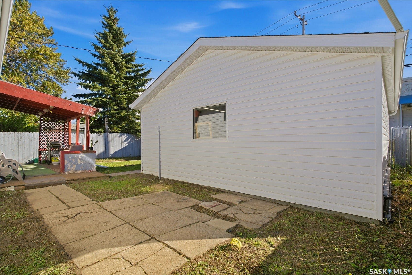 White siding garage structure, gravel hardscaping, covered patio with lattice, mature trees, and fenced perimeter