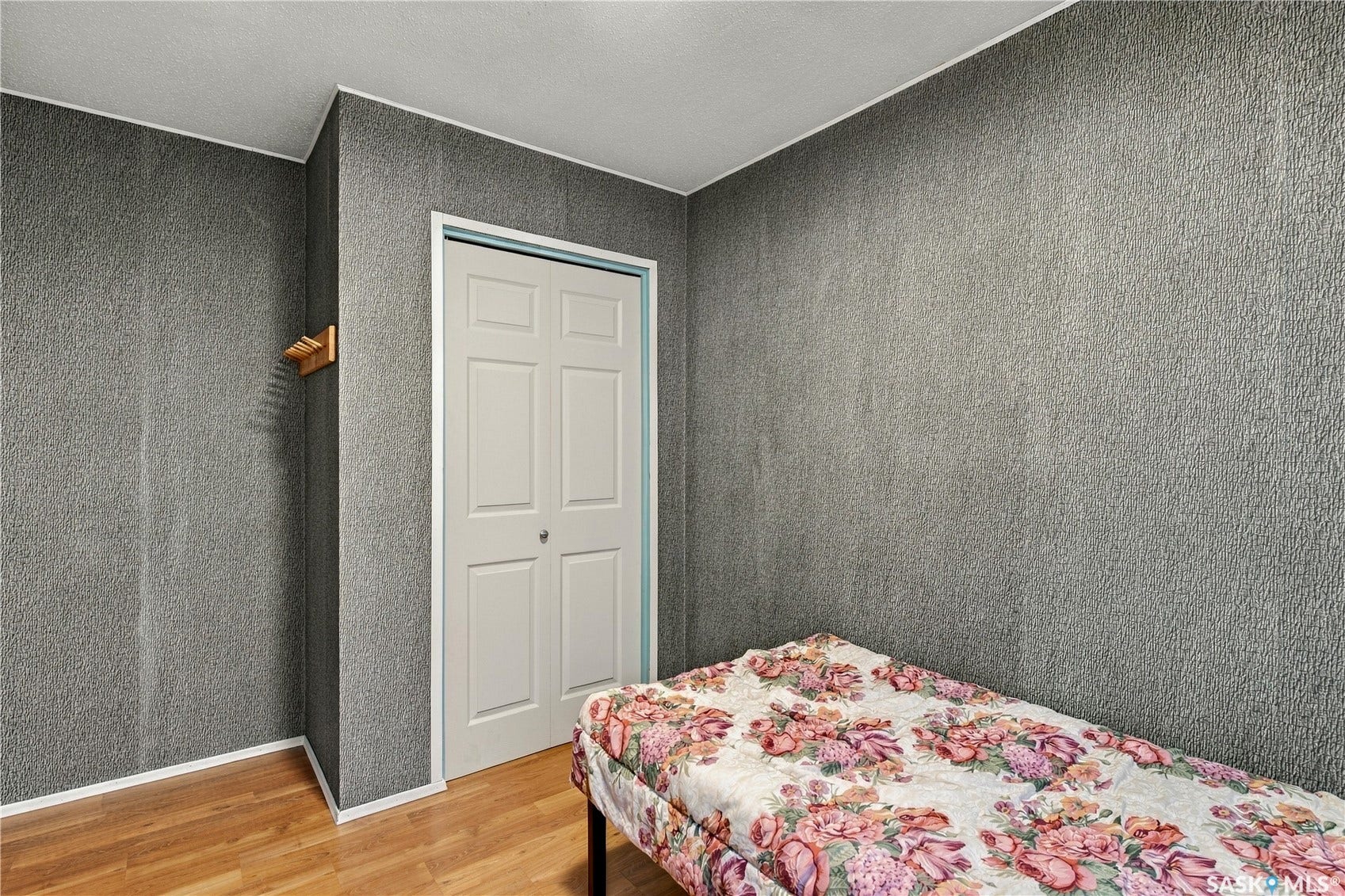 Textured wall covering with clean white trim, light wood-finish flooring, and a bi-fold closet door