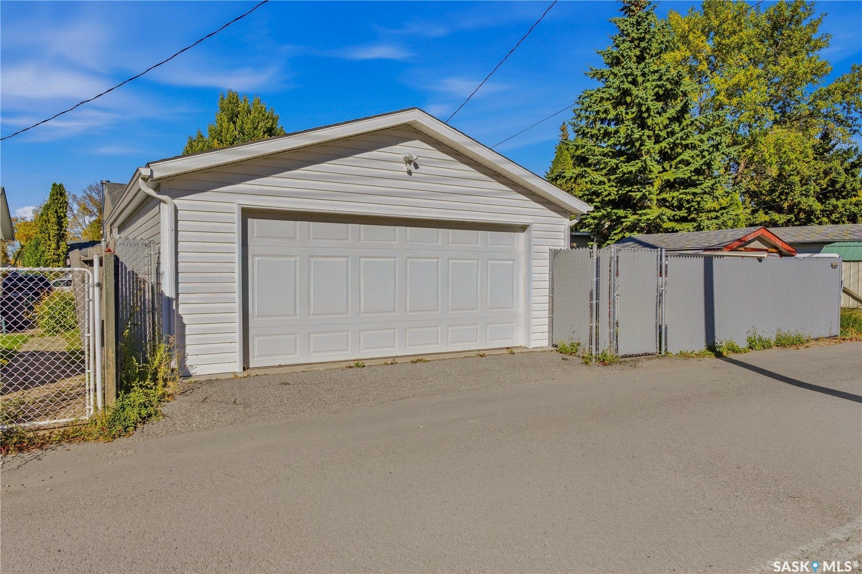 Detached garage with white siding, panel garage door, and chain link fencing