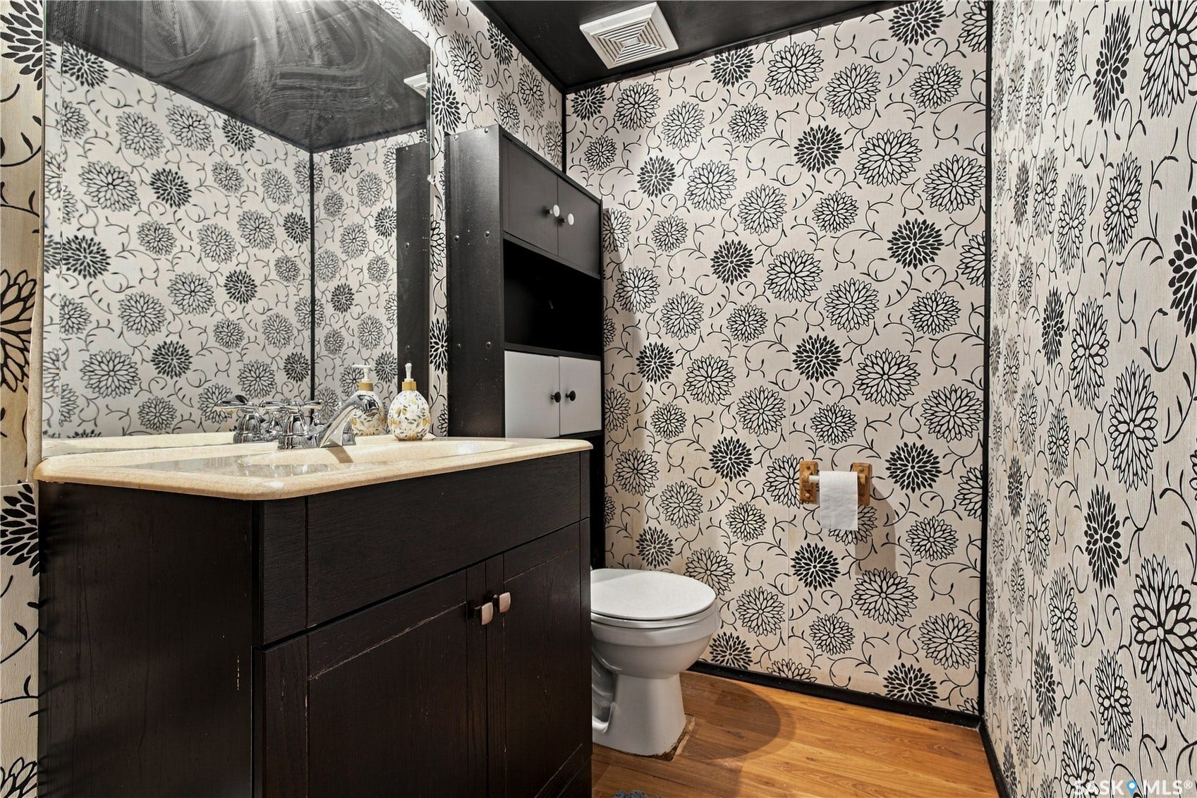 Wood-finish flooring with a toilet and a dark wood-finish vanity featuring a built-in sink and light-toned countertop