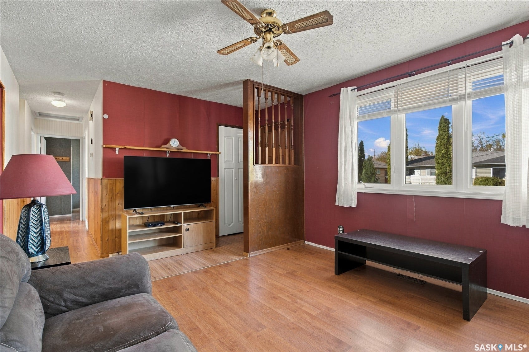 Wood-finish flooring throughout, ceiling fan with integrated lighting, wood paneling, and an expansive window with blinds