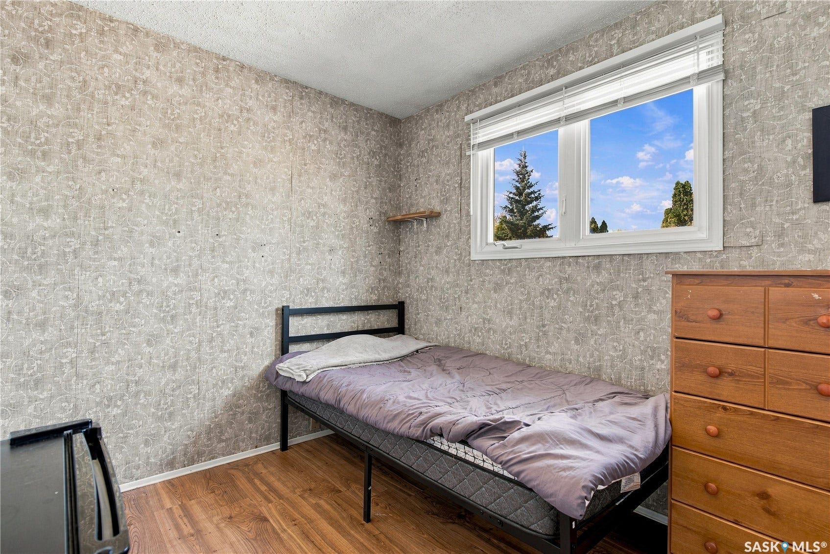 Large window with horizontal blinds, wood-finish flooring, and a wall-mounted shelf