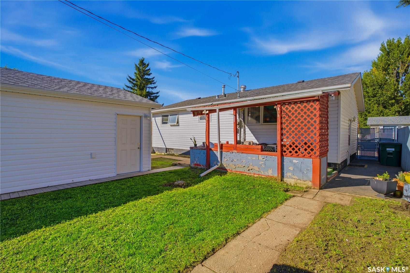 Detached garage with white siding, concrete walkway, and a covered back porch featuring a red lattice screen