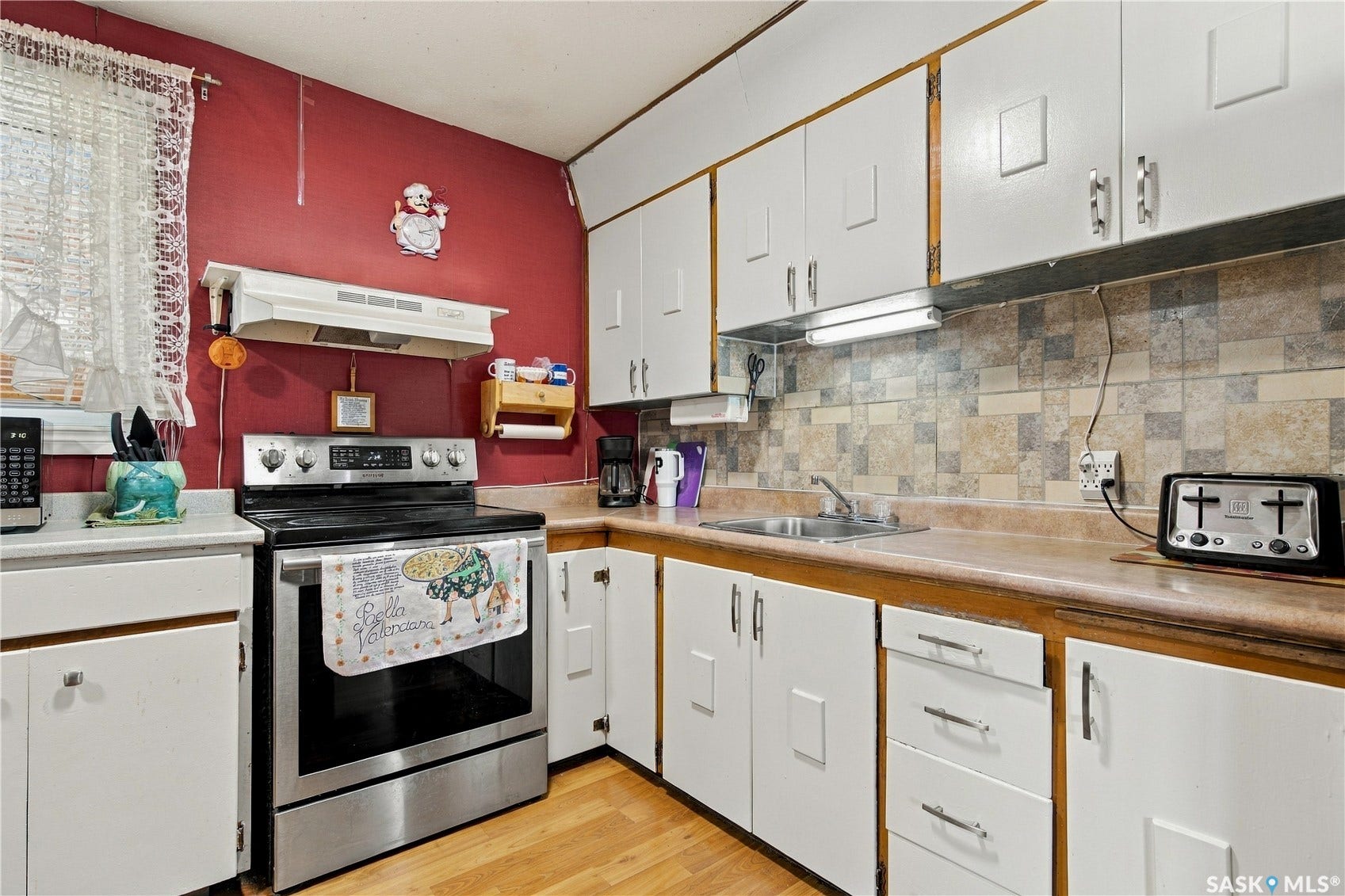 White cabinetry, stainless steel range, light wood-finish flooring, patterned tile backsplash, and a stainless steel sink