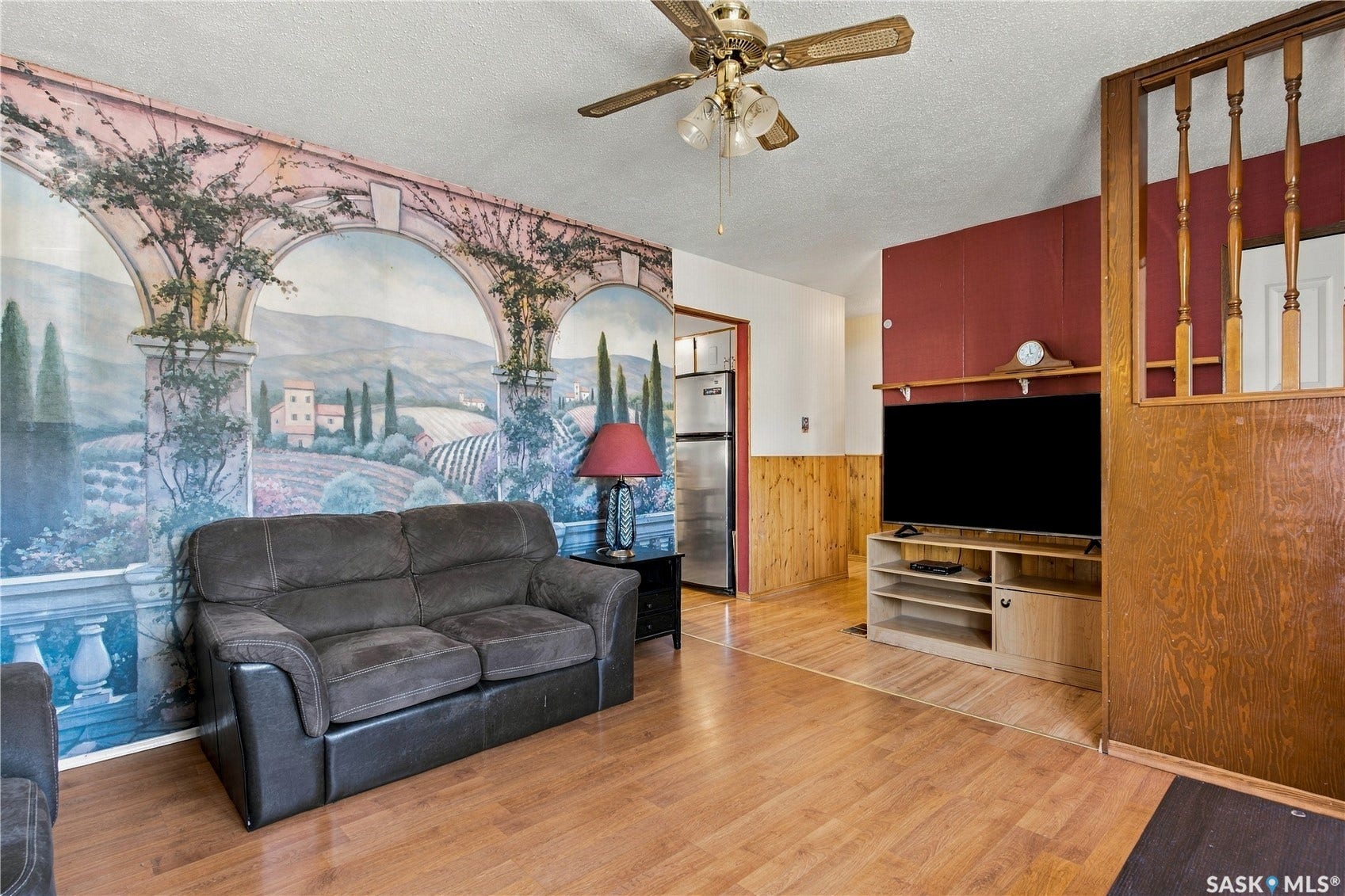 Wood-finish flooring throughout, with a decorative wall mural, and a ceiling fan with integrated lighting