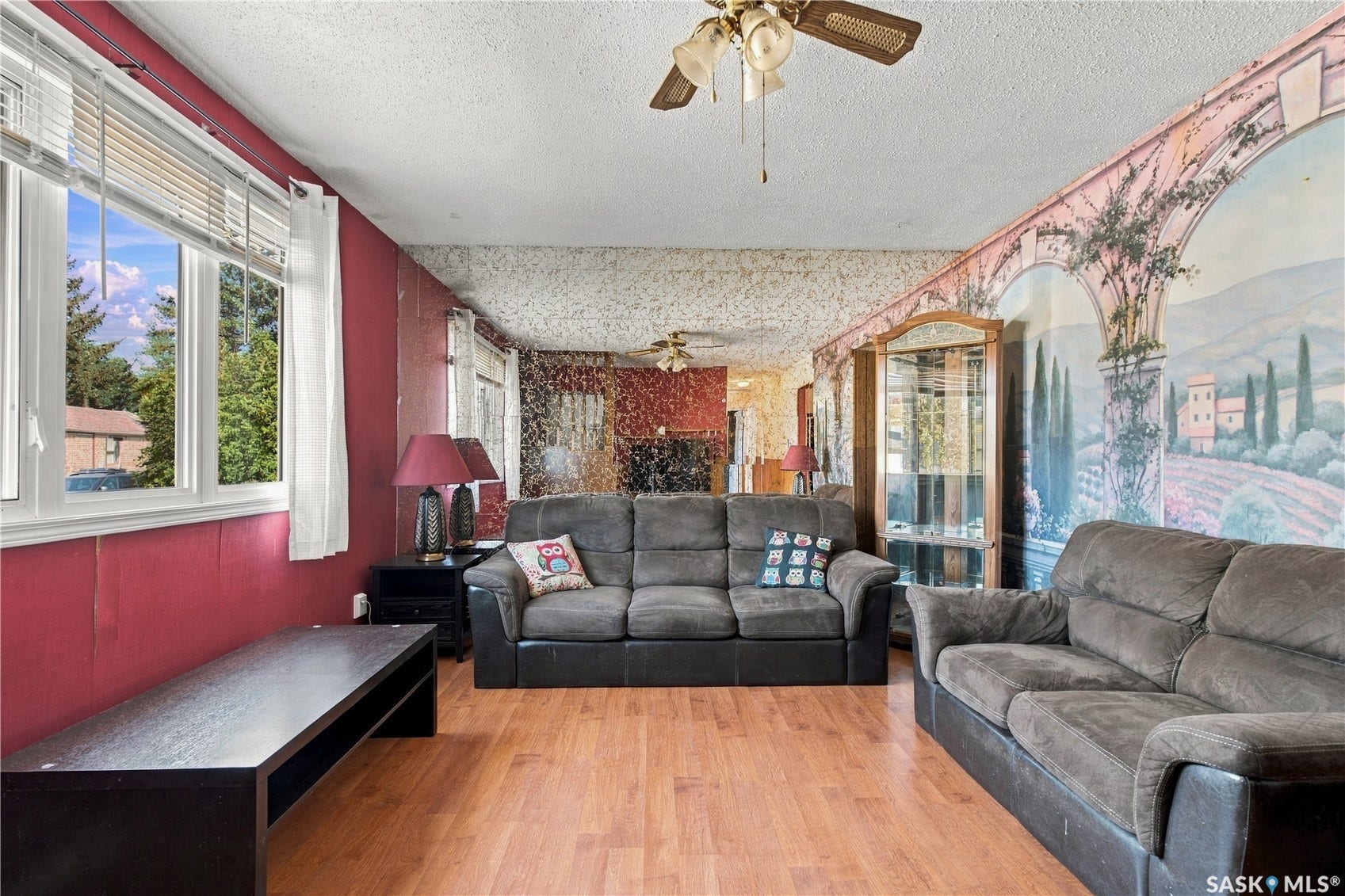 Wood-finish flooring, multiple windows with blinds, ceiling fan, and wall mural