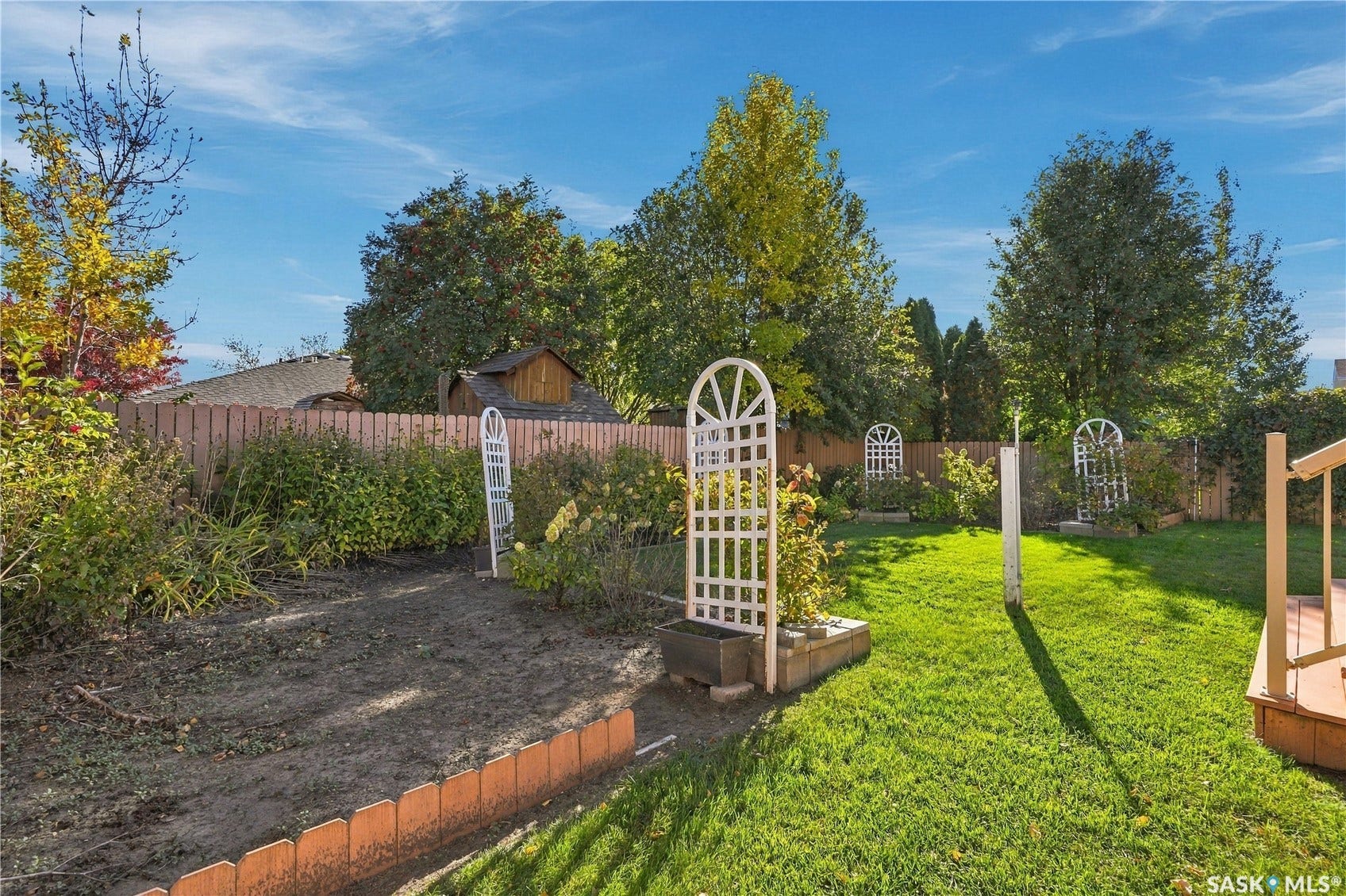 Expansive backyard featuring a manicured lawn, established landscaping, privacy fencing, and a wooden deck