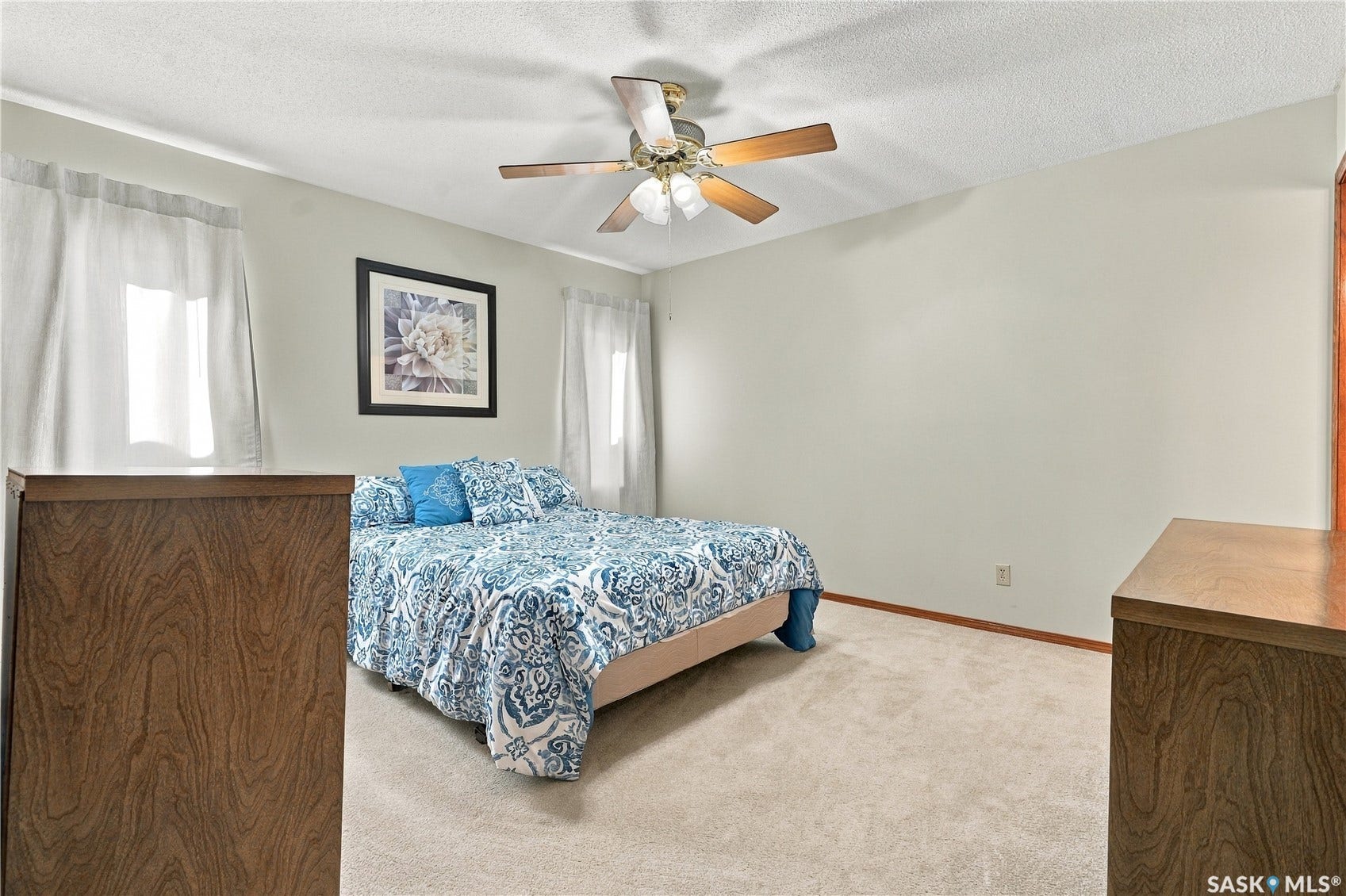 Ceiling fan with light fixture, neutral carpet flooring, two windows with white window treatments, and light-colored wall paint