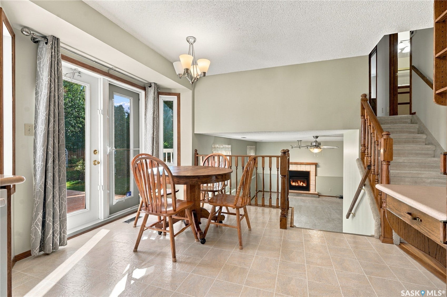 Dual French doors, bay window, tile flooring, wood staircase, and a lower-level fireplace with tile surround