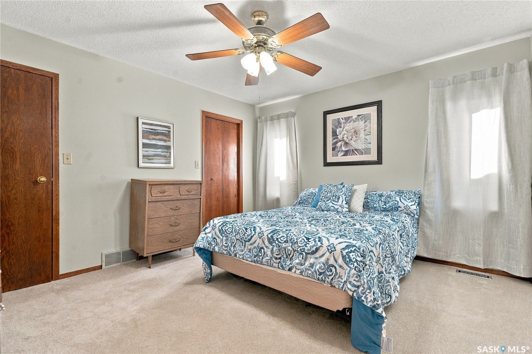 Neutral-toned walls, two wood-paneled doors, two windows with light-filtering curtains, and a ceiling fan with integrated lighting