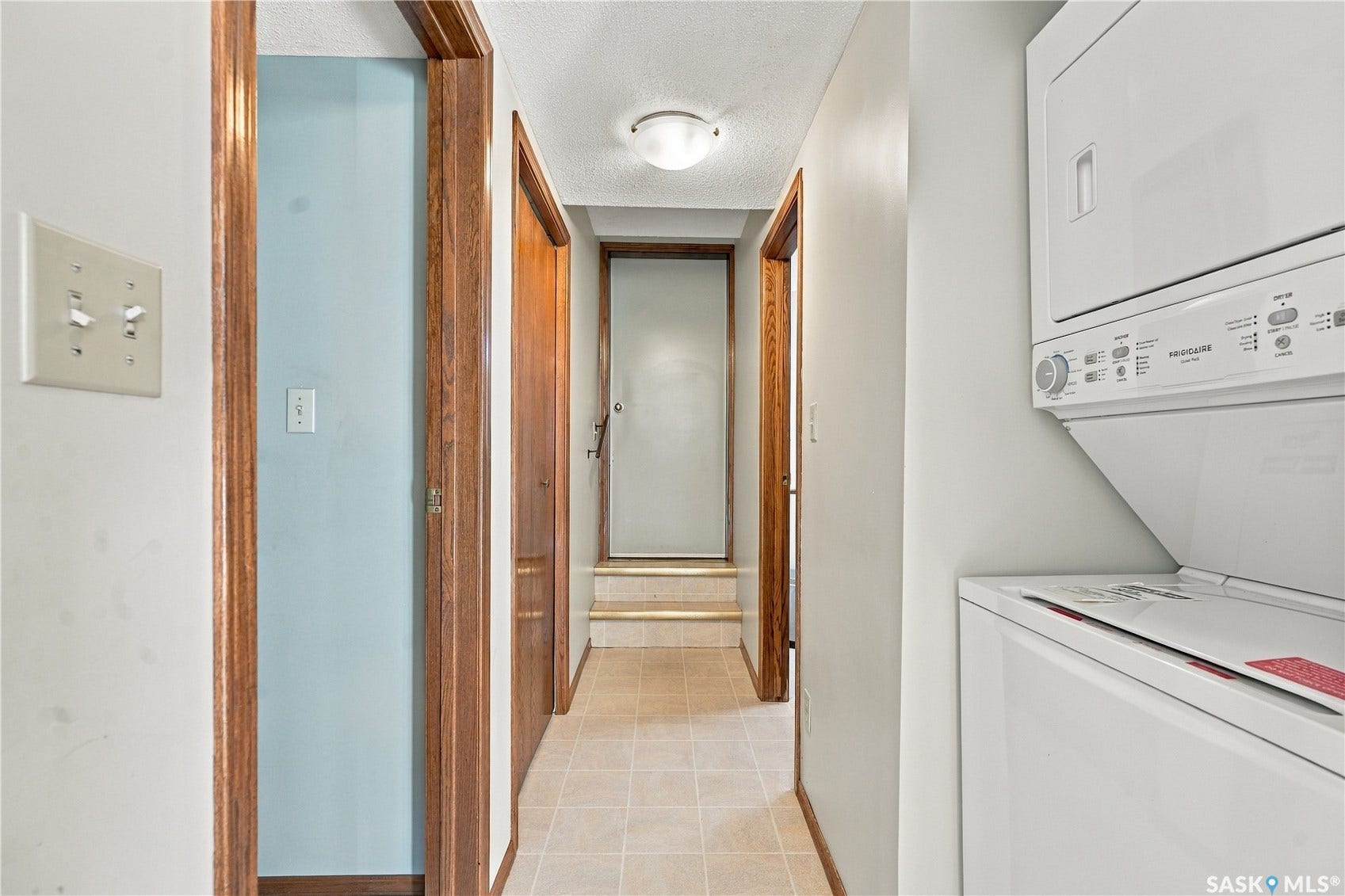 Hallway with tile flooring, wood trim, and a built-in stacked washer and dryer unit