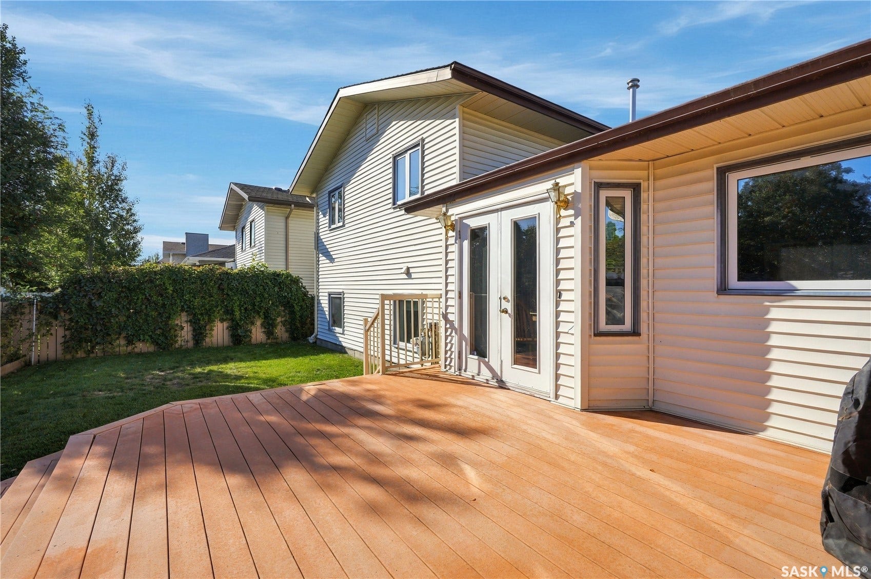 Expansive wood-finish deck with integrated steps, double pane glass doors, and light-colored siding exterior