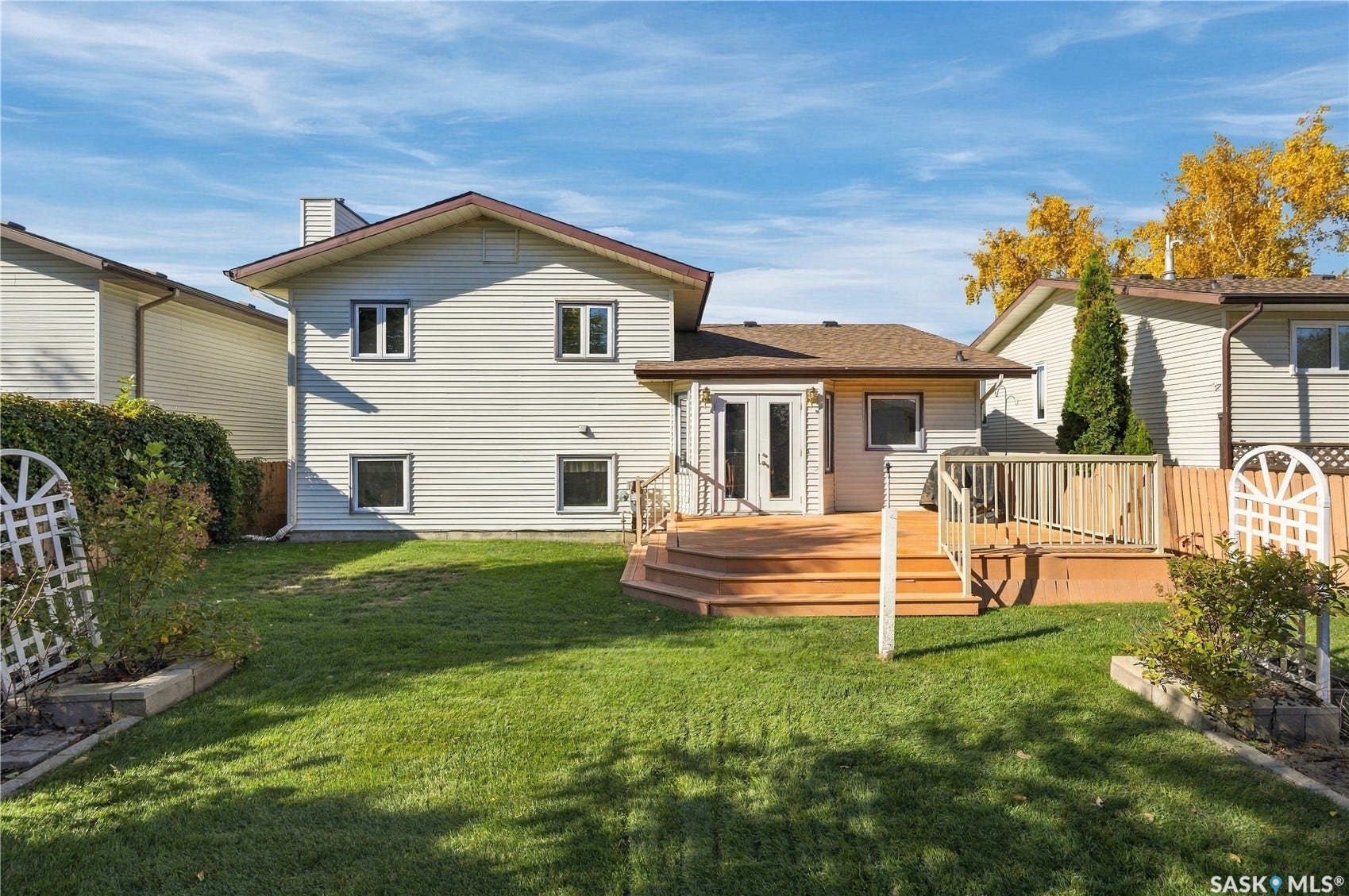 Multi-level wood deck, white vinyl siding, double French doors, wood fencing, and mature landscaping