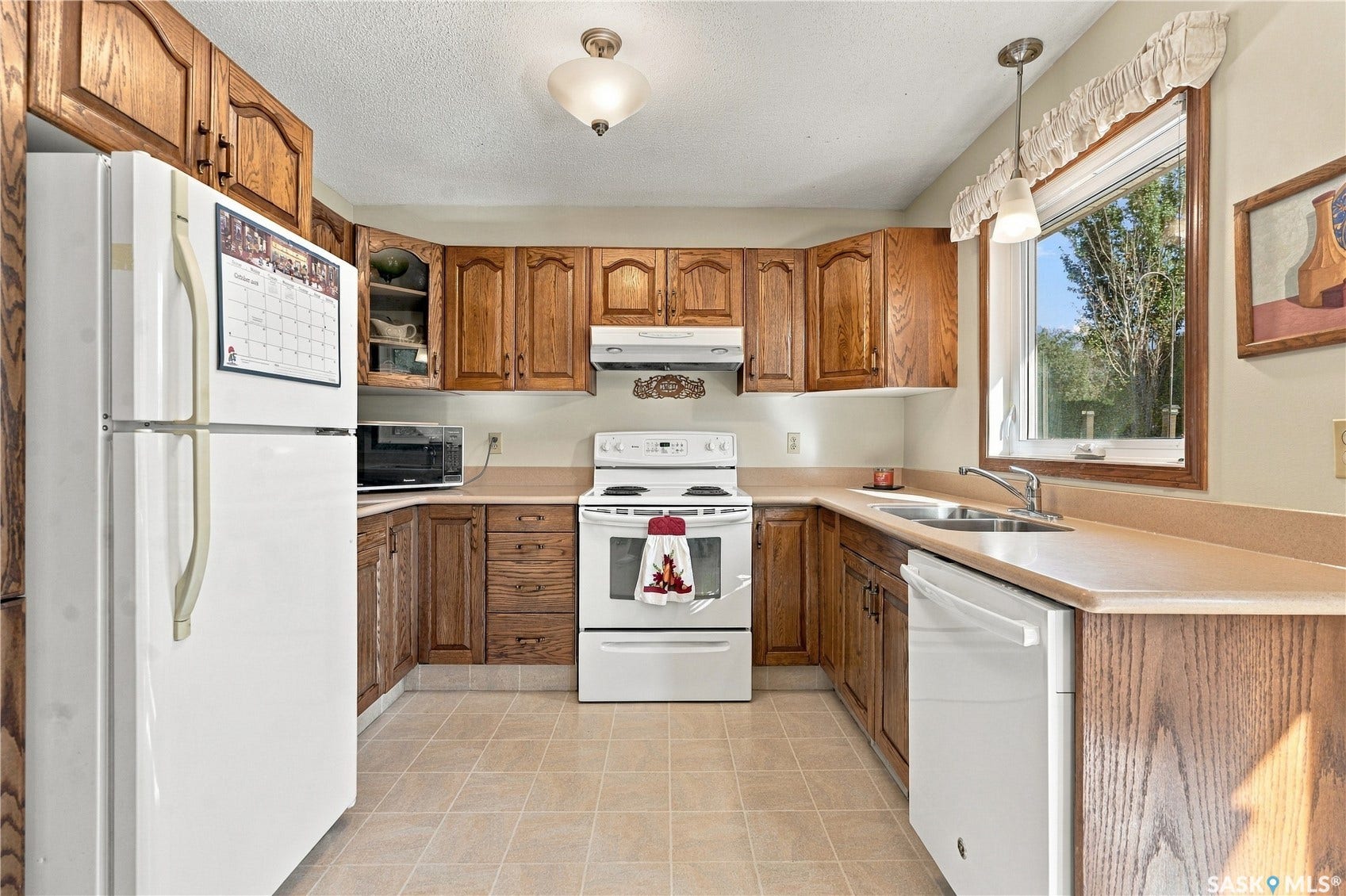 Kitchen featuring wood cabinetry, white appliances, light-toned countertops, and tile flooring