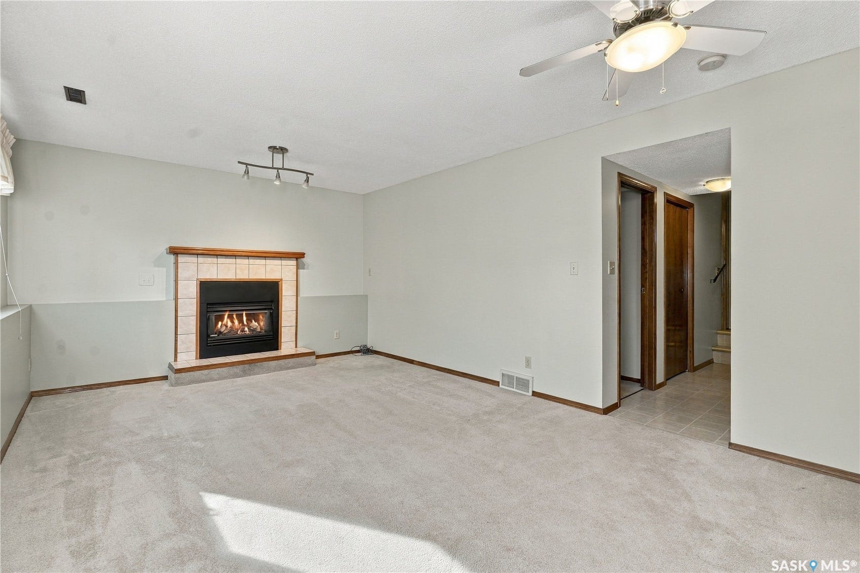 Built-in fireplace with a tile surround and wood mantel, track lighting, carpeted flooring, and a ceiling fan with integrated lighting