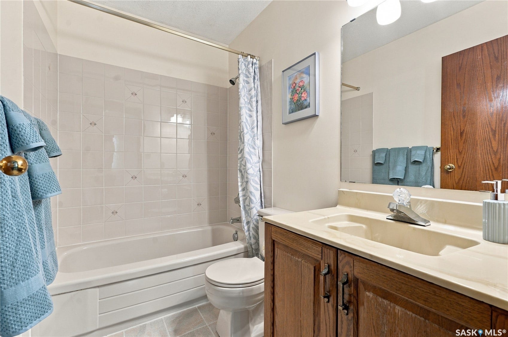 Bathtub with tiled surround, wood-finish vanity with an integrated sink, and a wall-mounted mirror