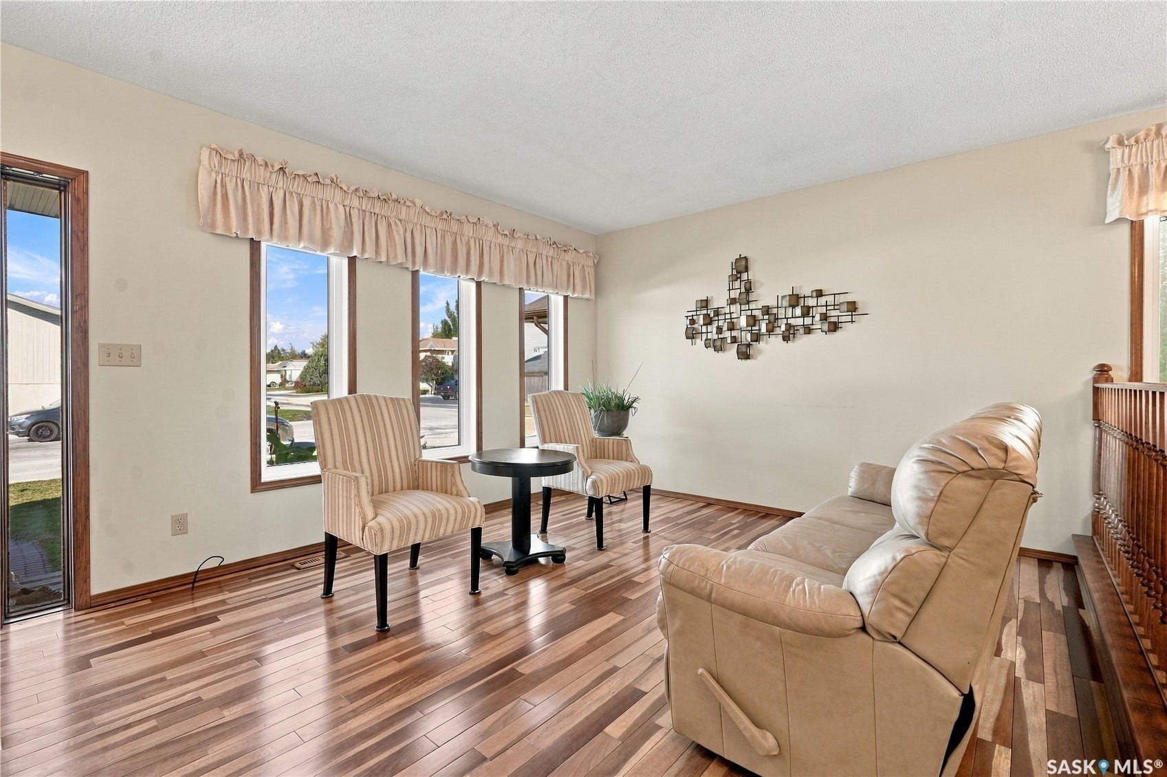Wood-finish flooring throughout, light-colored wall paint, multiple windows with trim, and a wood banister