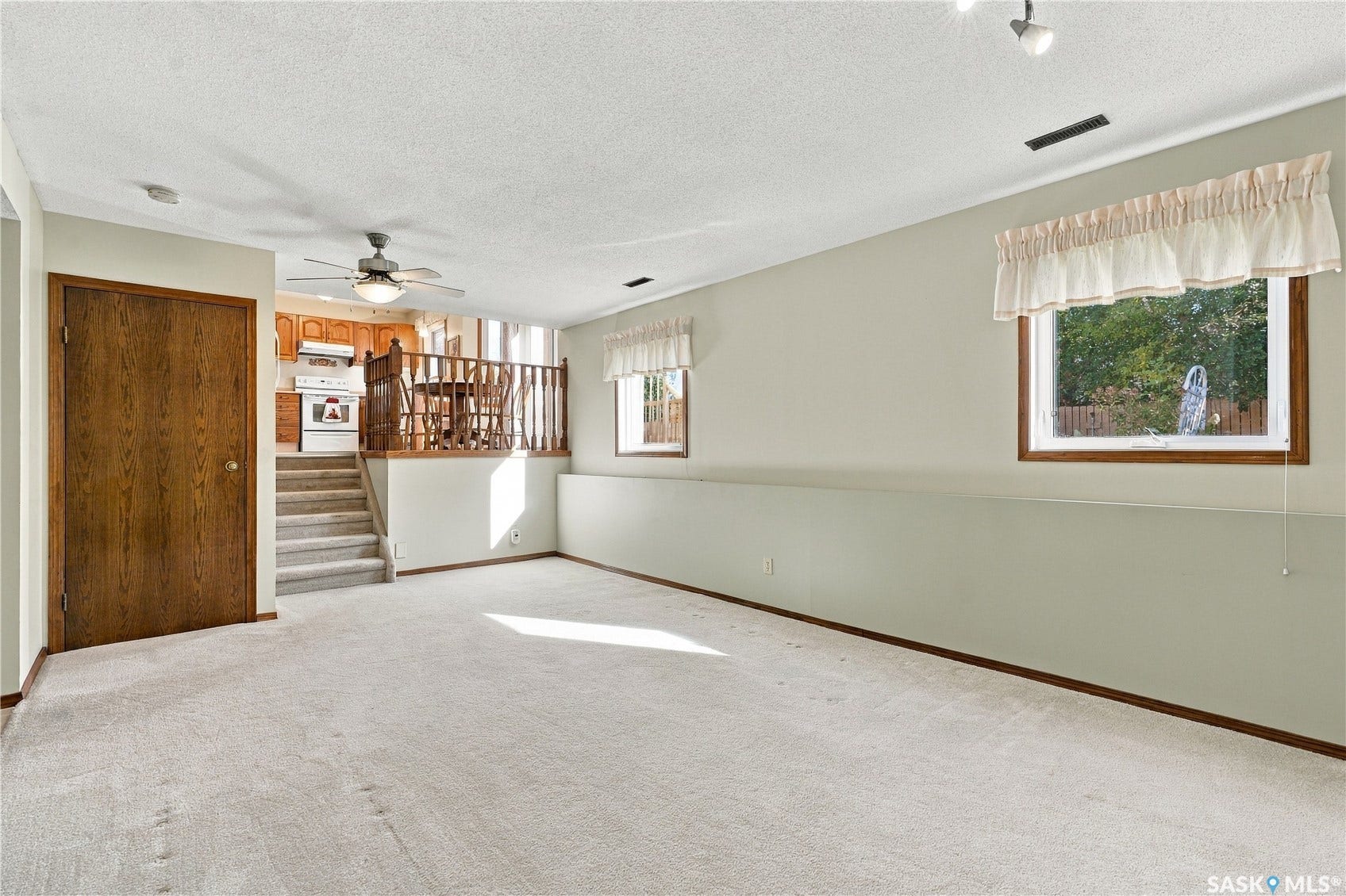 Carpeted living area with two windows, a ceiling fan, and a wood-finish door