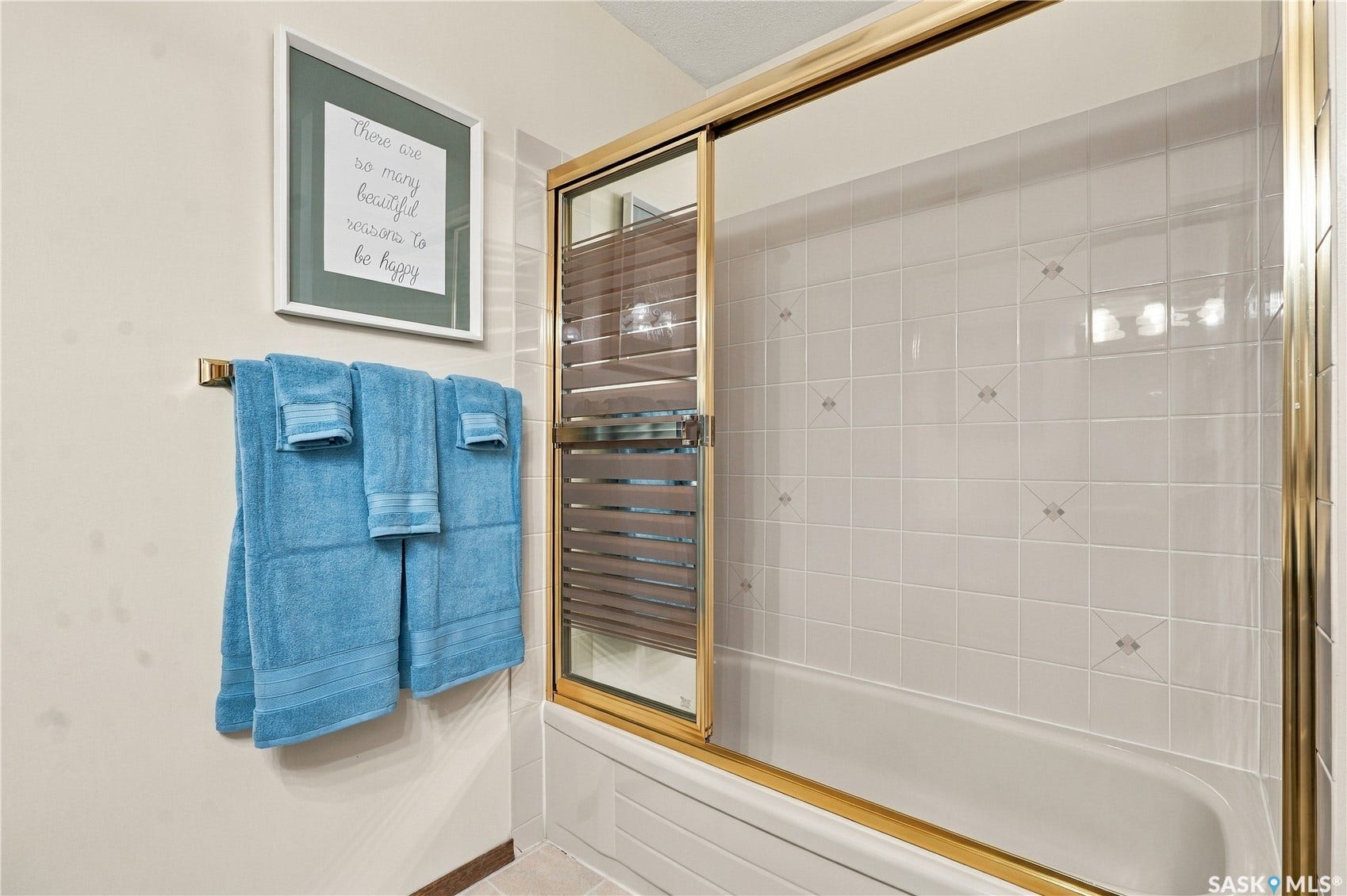 Bathtub with gold-finish sliding glass enclosure, white square wall tiling, and decorative inlay accents