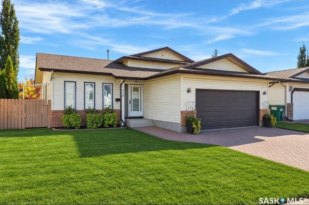 Expansive front lawn, paved driveway, attached two-car garage, and a light-colored exterior with brick accents