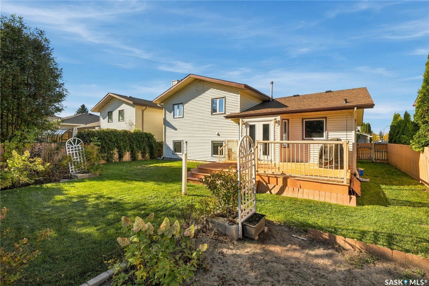 Expansive grassy yard with mature shrubs, featuring a wood deck with railings, and a privacy fence