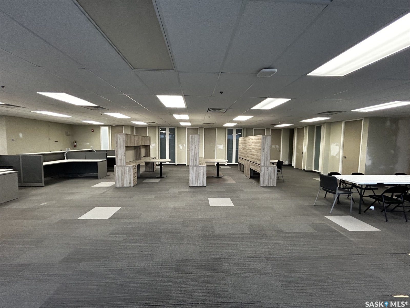 Expansive open-plan office space featuring modular carpet flooring, acoustic tile ceiling, and fluorescent lighting fixtures
