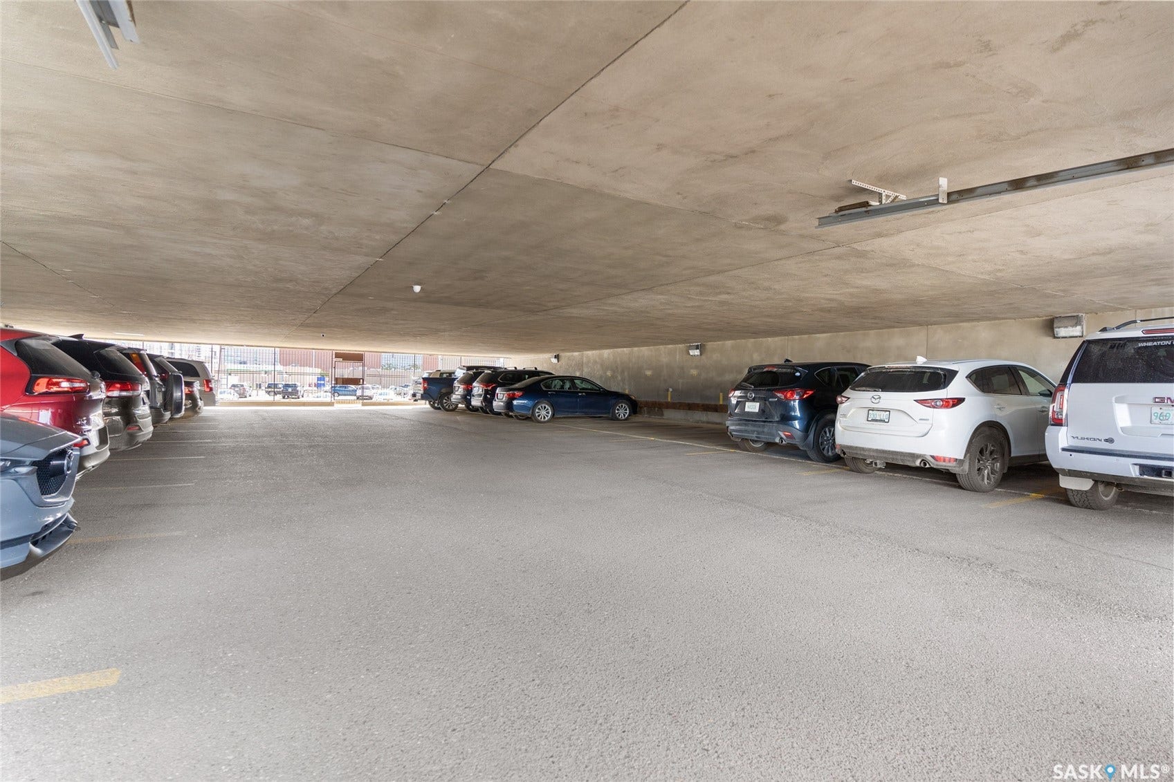 Covered parking area with concrete ceiling and wall finishes, illuminated by recessed lighting fixtures