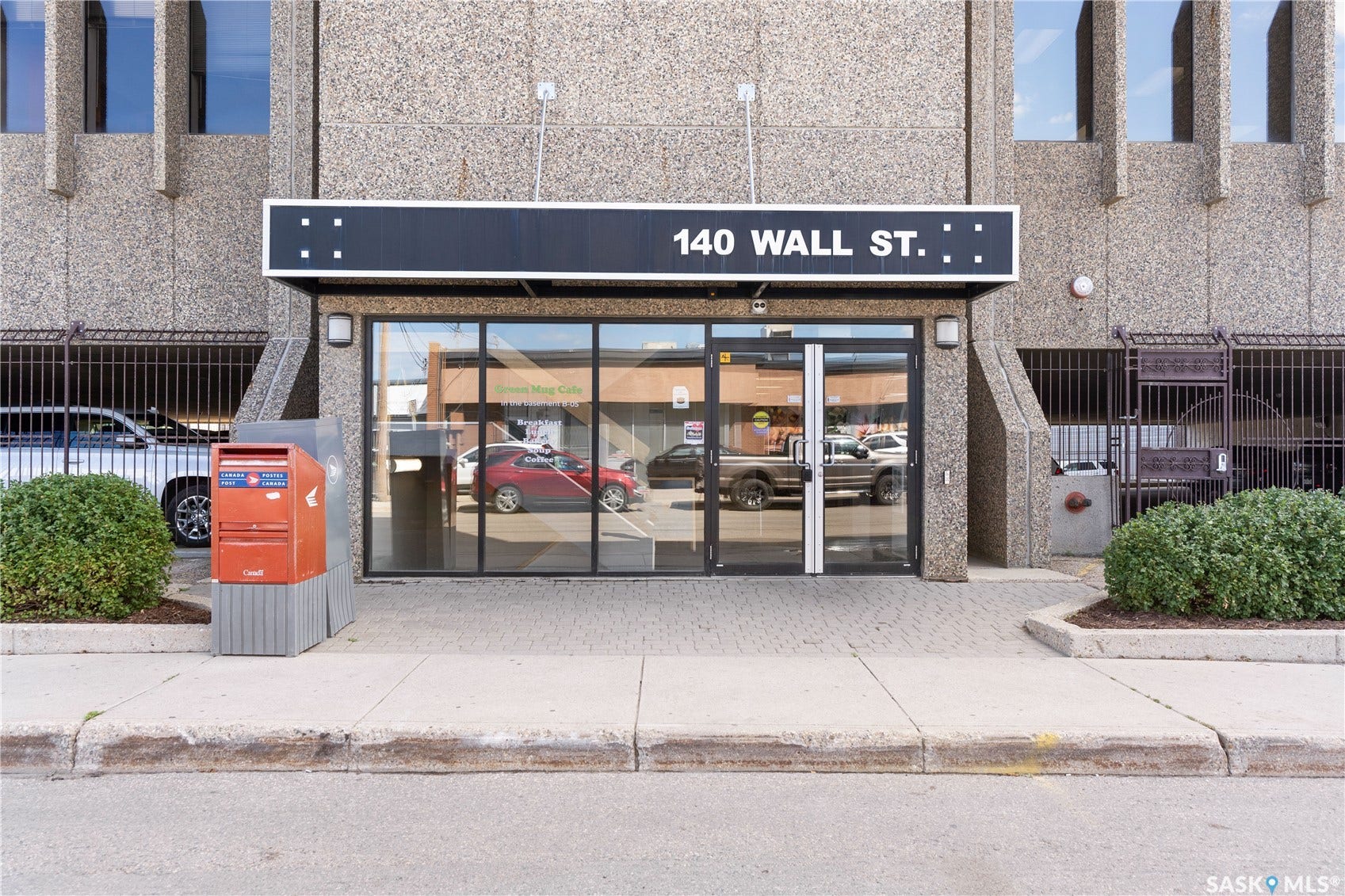 Building entrance featuring full-pane glass doors, a prominent address sign, and textured concrete exterior