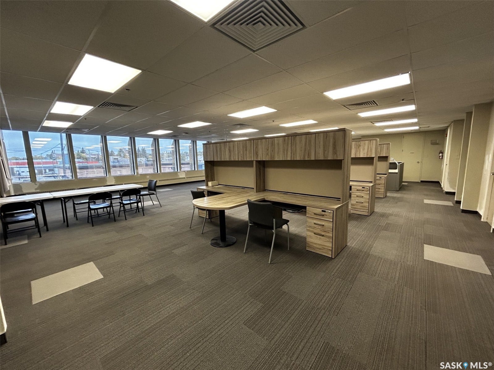 Expansive open-plan office space featuring carpet tile flooring, full-height windows, and acoustic tile ceiling