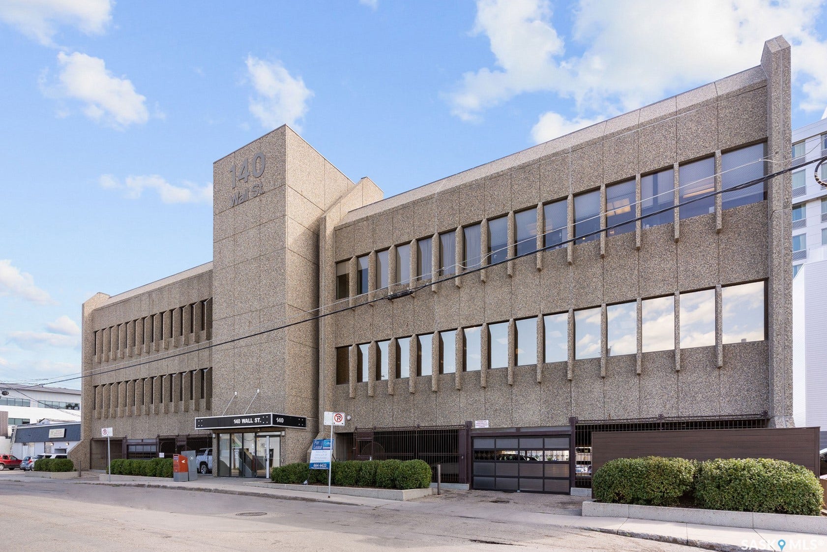 Concrete facade with multiple window banks, ground-level entrance with signage, and an integrated garage door