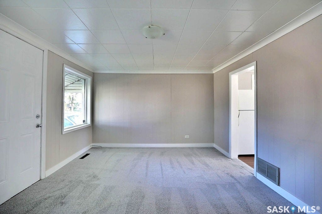 Wall-to-wall carpeting in a neutral tone, an entry door with hardware, a window with white trim, and a ceiling-mounted light fixture