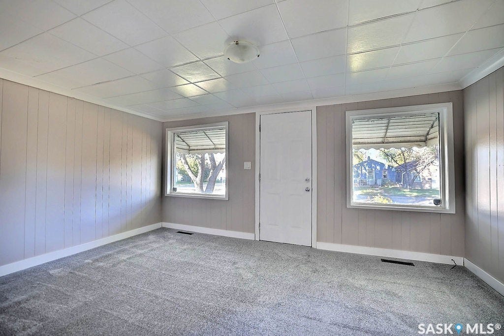 Neutral-toned paneled walls with crown molding, two windows with white trim, a white door, and textured carpet flooring