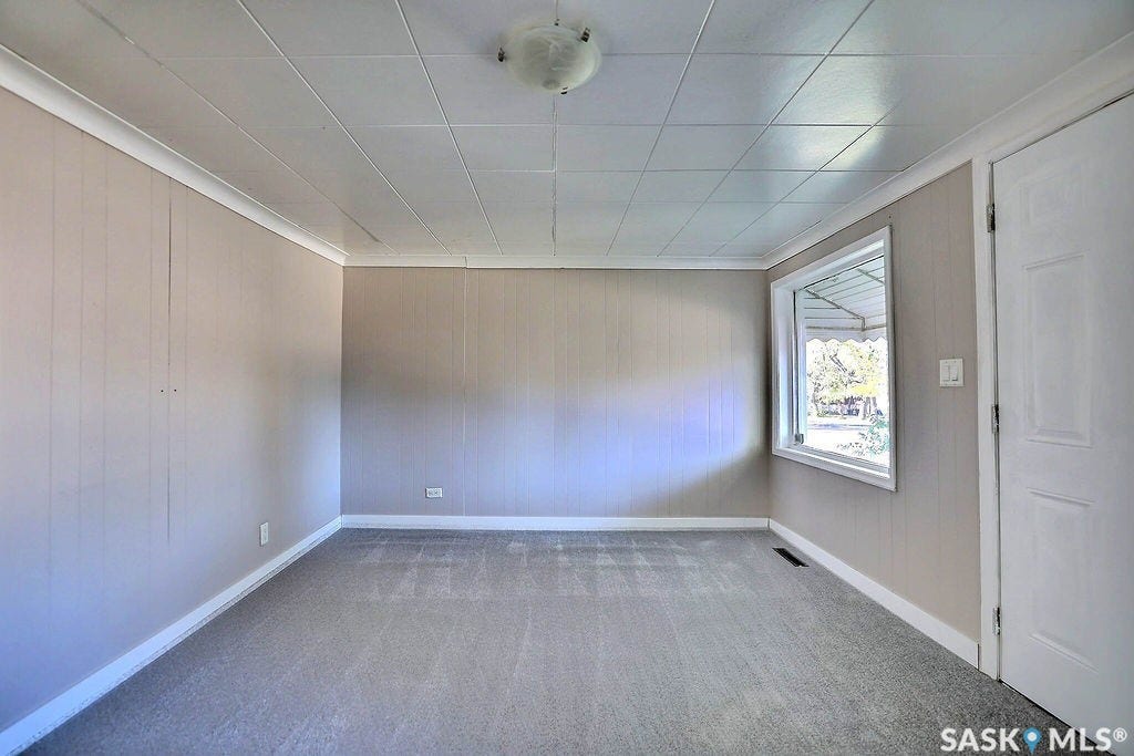 Light gray paneled walls, gray carpeting, white trim, and a window providing natural illumination