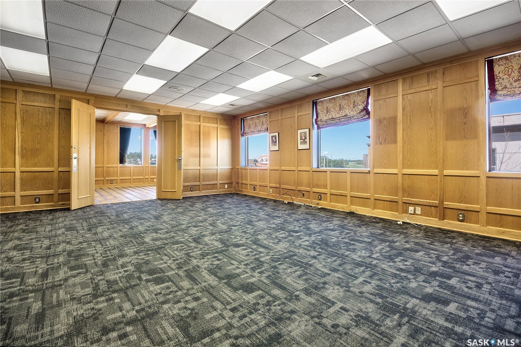 Wood paneling, drop ceiling with integrated lighting, patterned carpet flooring, and multiple windows