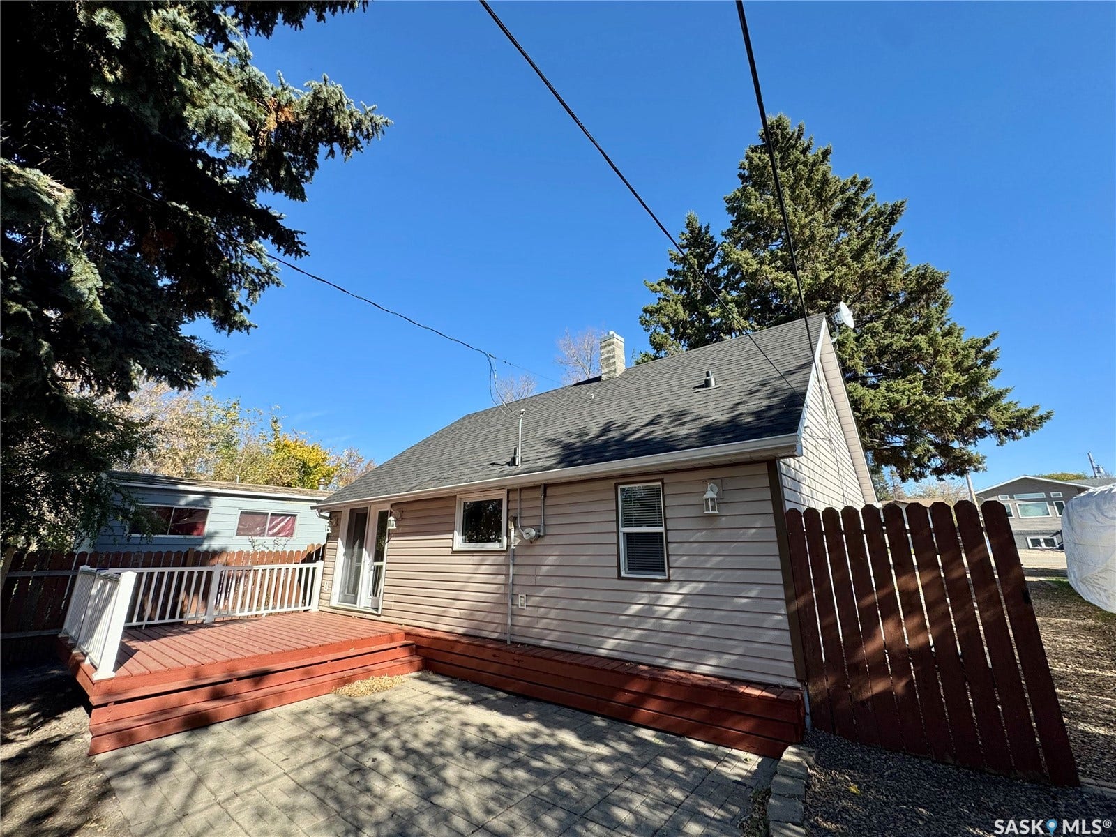 365 Keats Street, Southey SK S0G 4P0 Back exterior featuring a pitched roof, light-colored siding, a wood deck with white railings, and a paved patio area