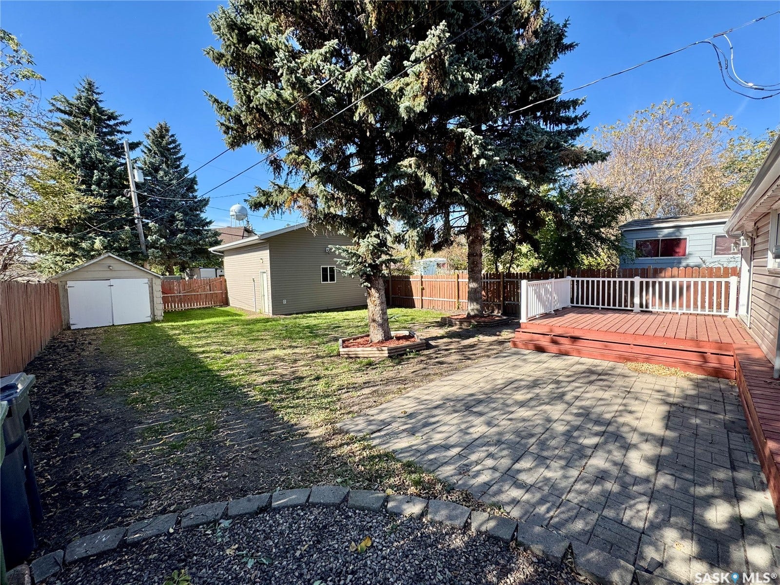 365 Keats Street, Southey SK S0G 4P0 Spacious backyard featuring a paver patio, elevated wood deck with white railing, wood fencing, and a detached garage