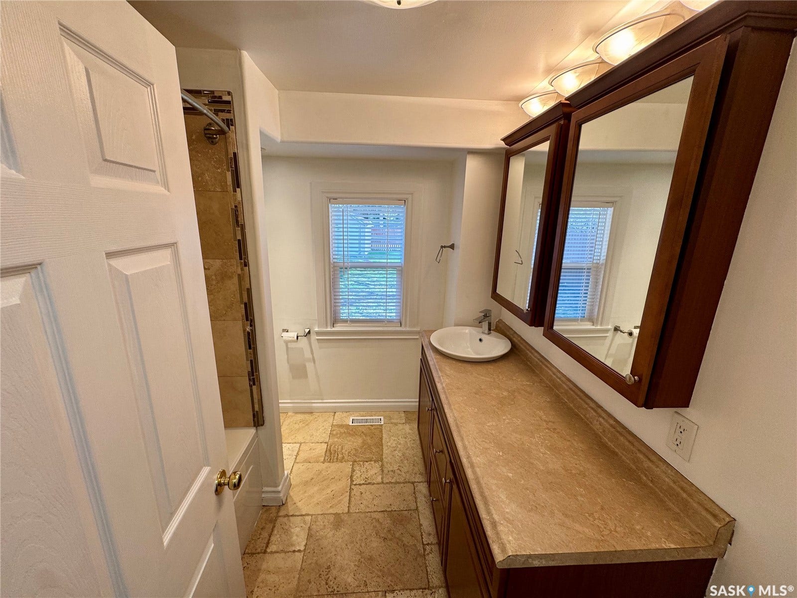 365 Keats Street, Southey SK S0G 4P0 Warm-toned tiled flooring, a built-in vanity with a countertop, an integrated sink, and mirrored medicine cabinets