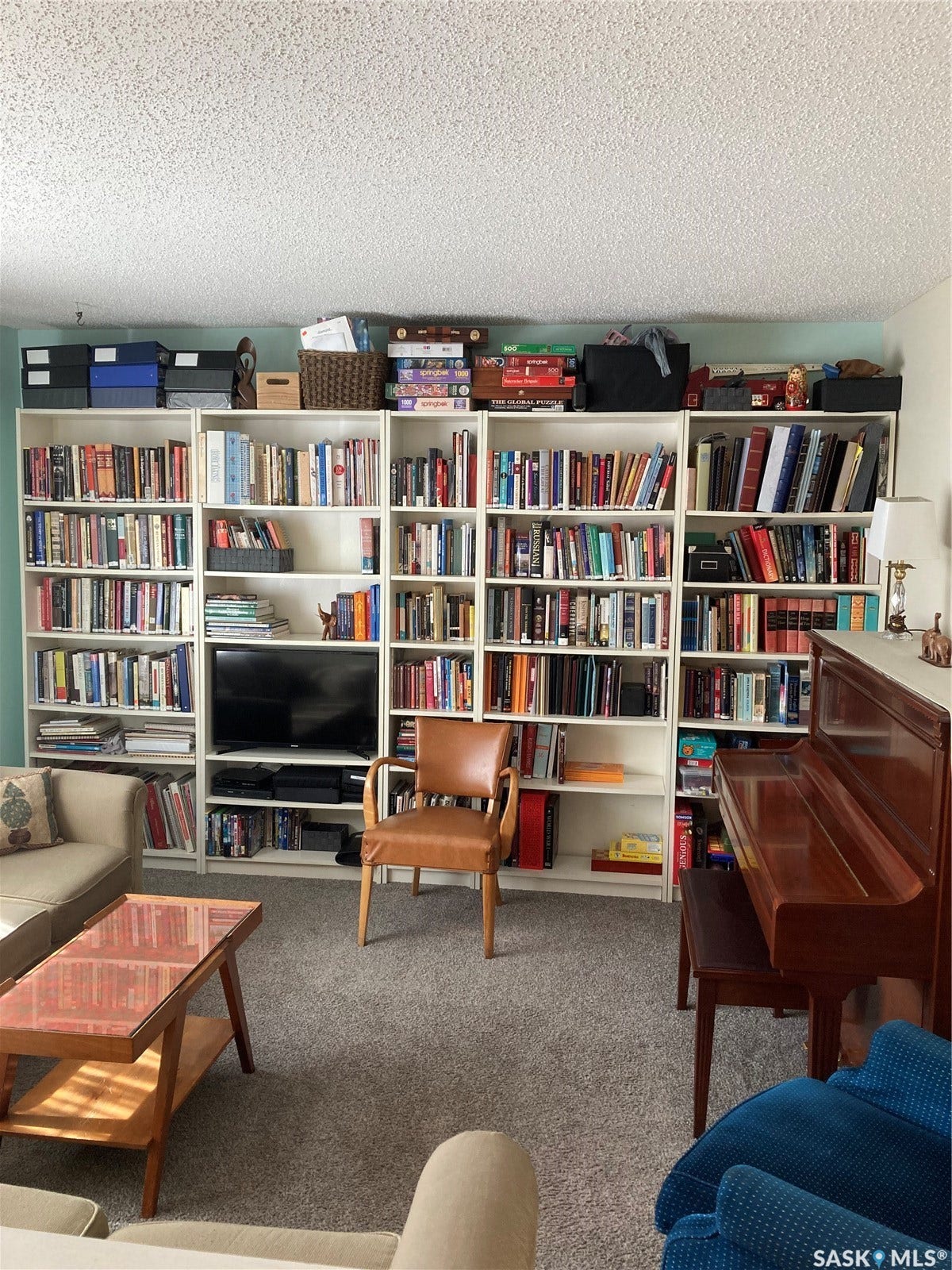 Full-wall built-in shelving with integrated media space, light-colored carpeting, and a wood-finish upright piano