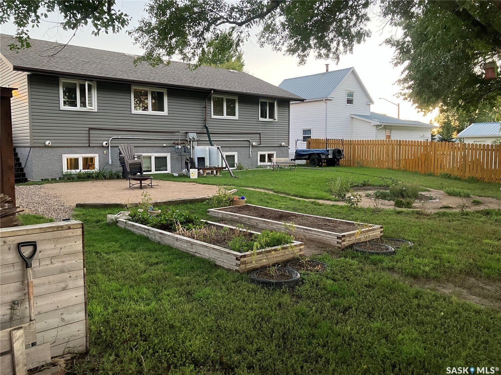 Expansive backyard featuring a gravel patio, raised garden beds, wood fencing, and a mature tree