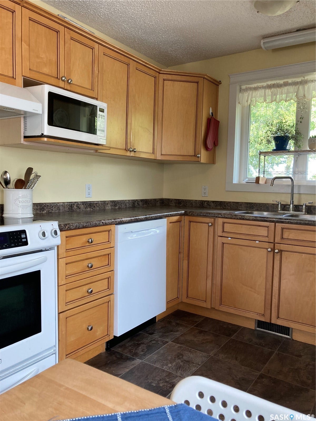 Wood-finish cabinetry, solid surface countertops, built-in dishwasher, white range, and a window with a stainless steel sink