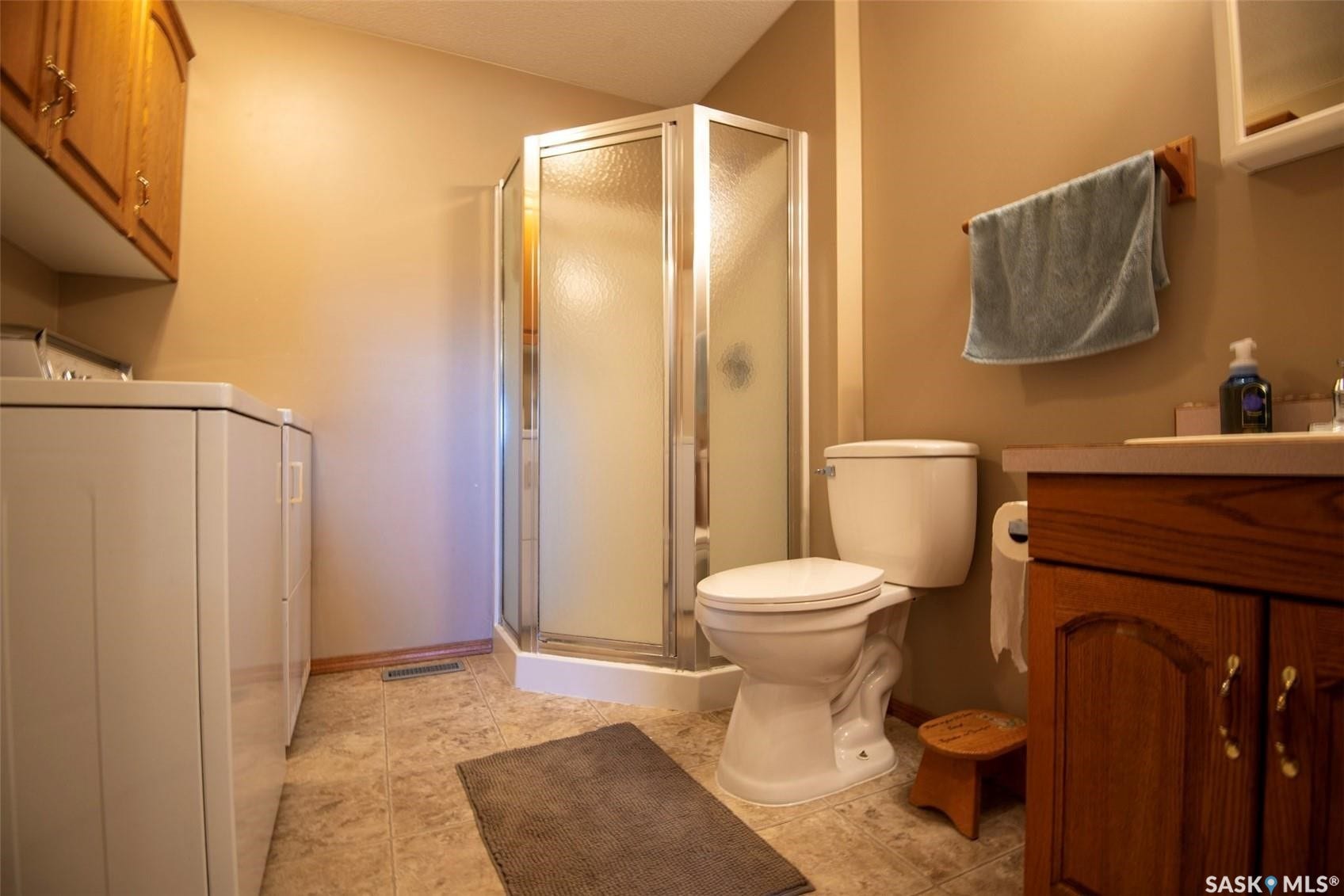 Combines Bath/Laundry. Shower enclosure with textured glass panels, wood-finish vanity with countertop, and overhead wood-finish cabinetry