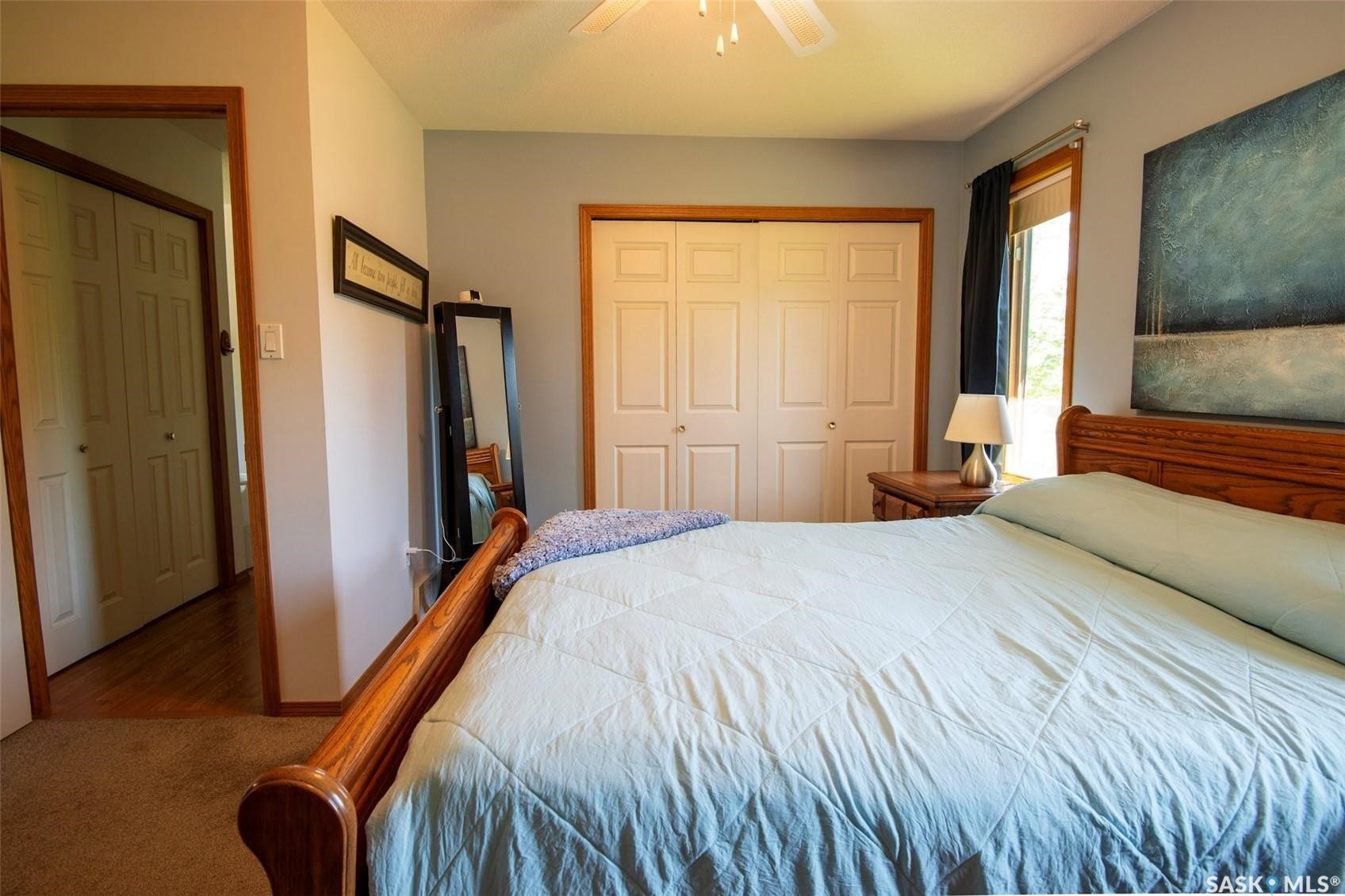 Built-in closet with bi-fold doors, natural wood trim, window with privacy curtains, and a ceiling fan