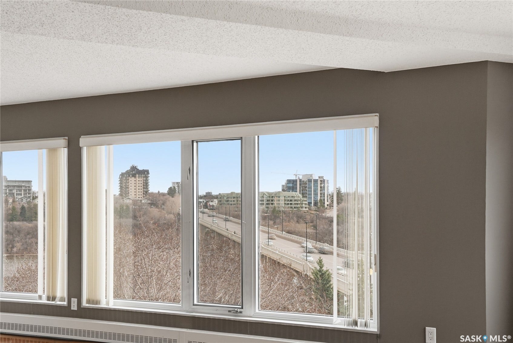 Expansive window wall with vertical blinds, presenting broad urban and natural elements