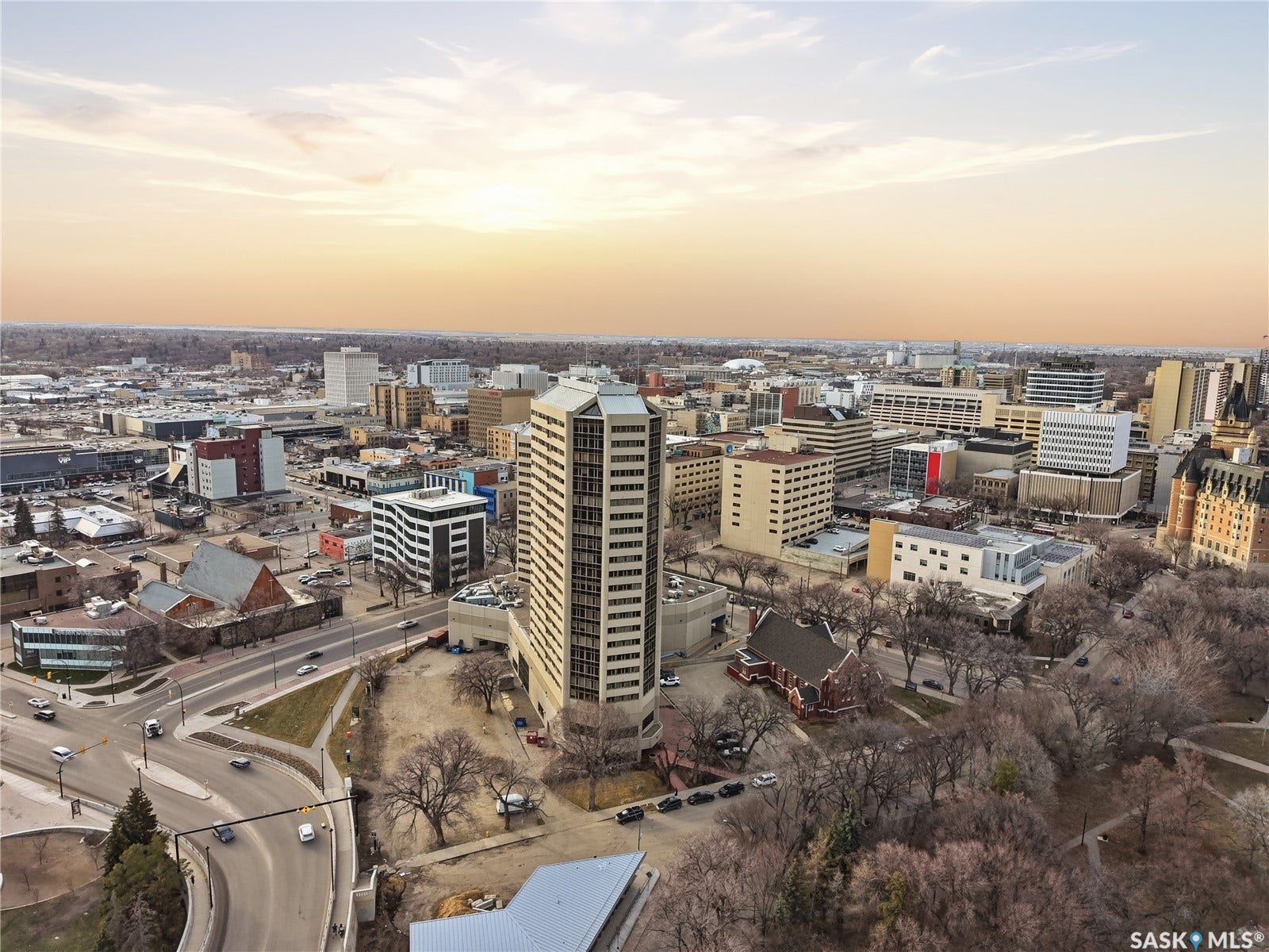 Expansive urban landscape featuring diverse architectural styles, a prominent high-rise building, surrounding mature trees, and visible roadways