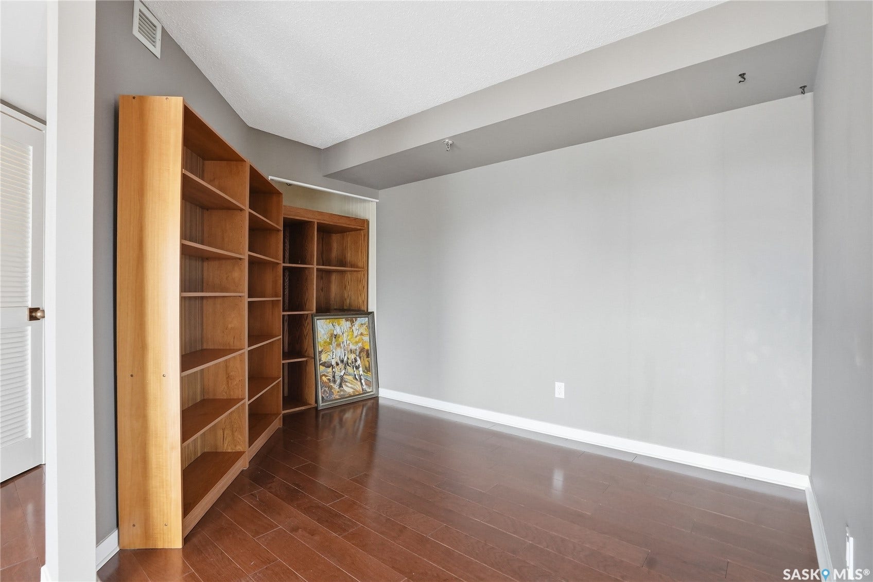 Rich wood-finish flooring, built-in shelving, neutral wall tones, and overhead lighting
