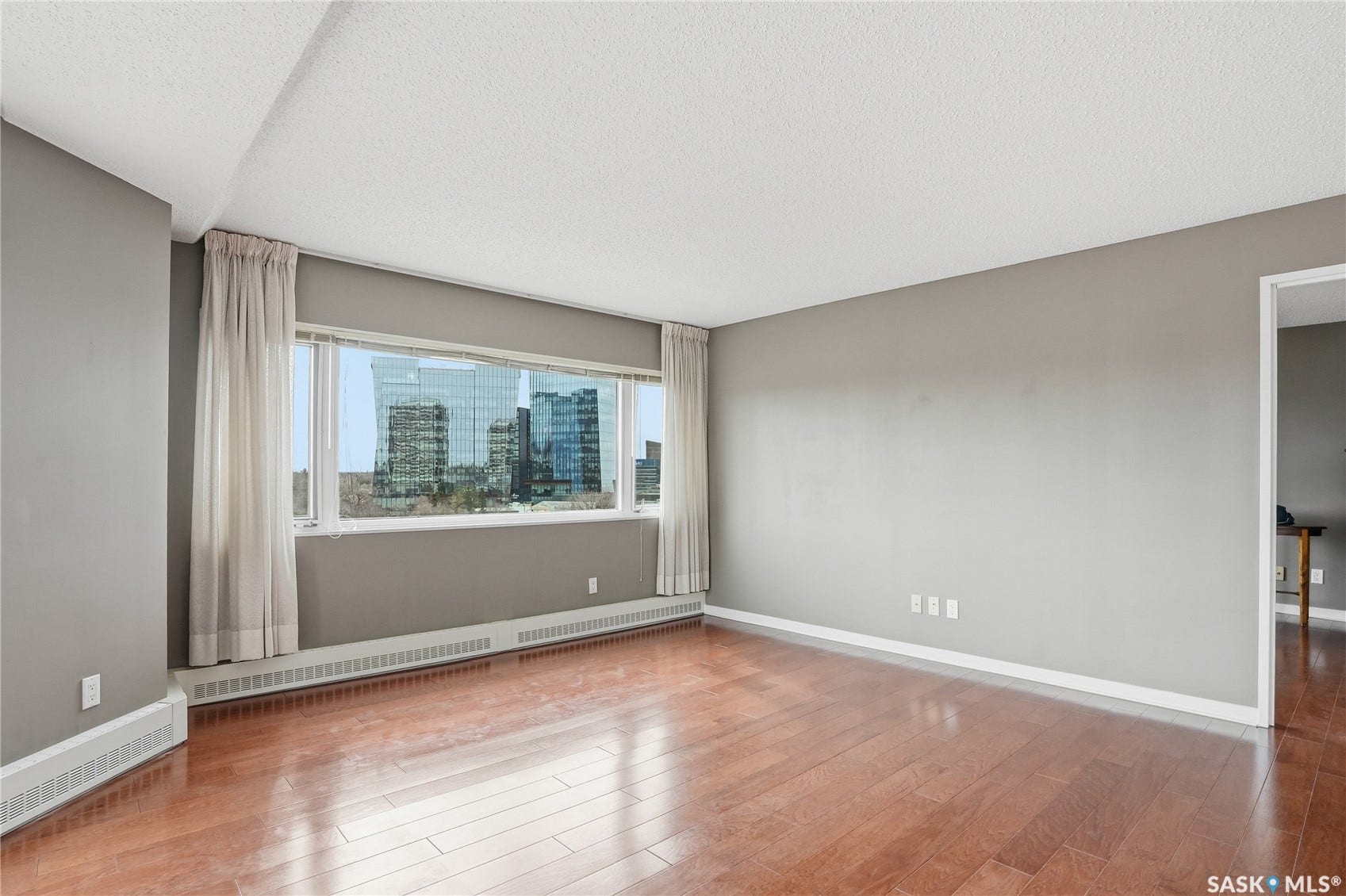 Wide window offering urban scenery, warm wood-finish flooring, and neutral wall tones