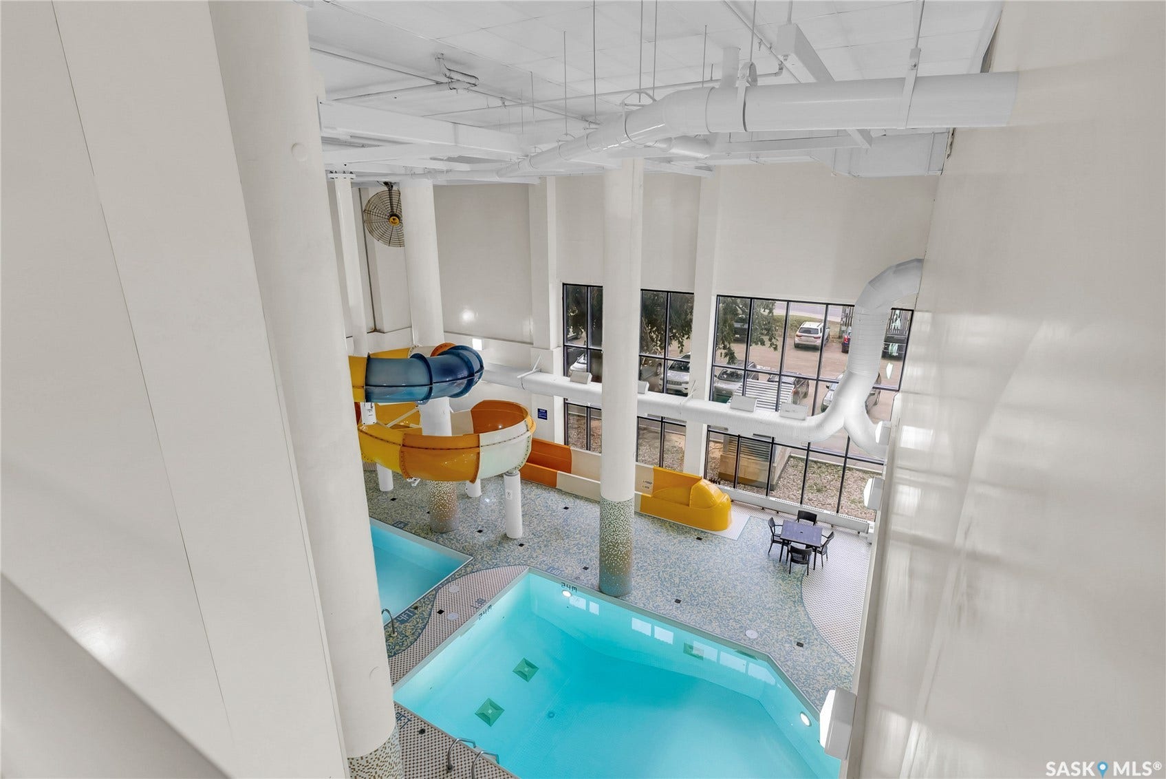 Indoor aquatic area featuring two pools, a water slide, and abundant natural light from large windows